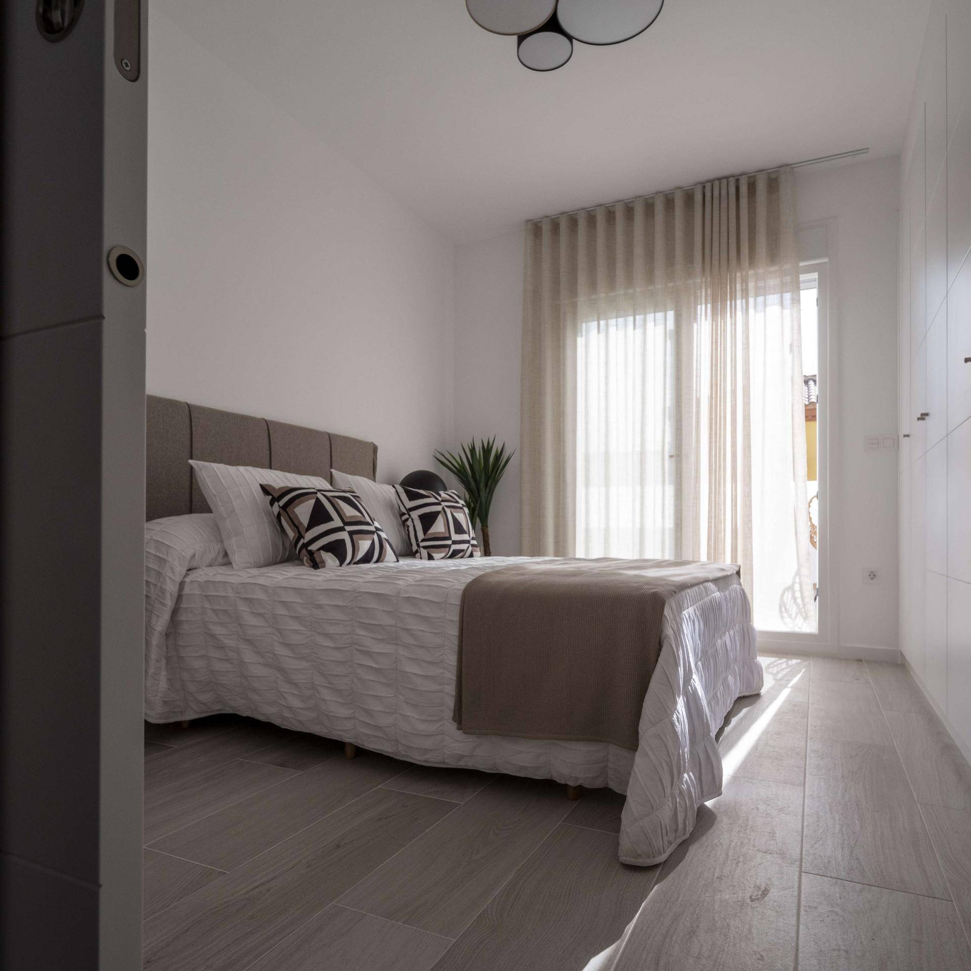 Helles Schlafzimmer mit Doppelbett, weißen Einbauschränken und Zugang zur Terrasse.