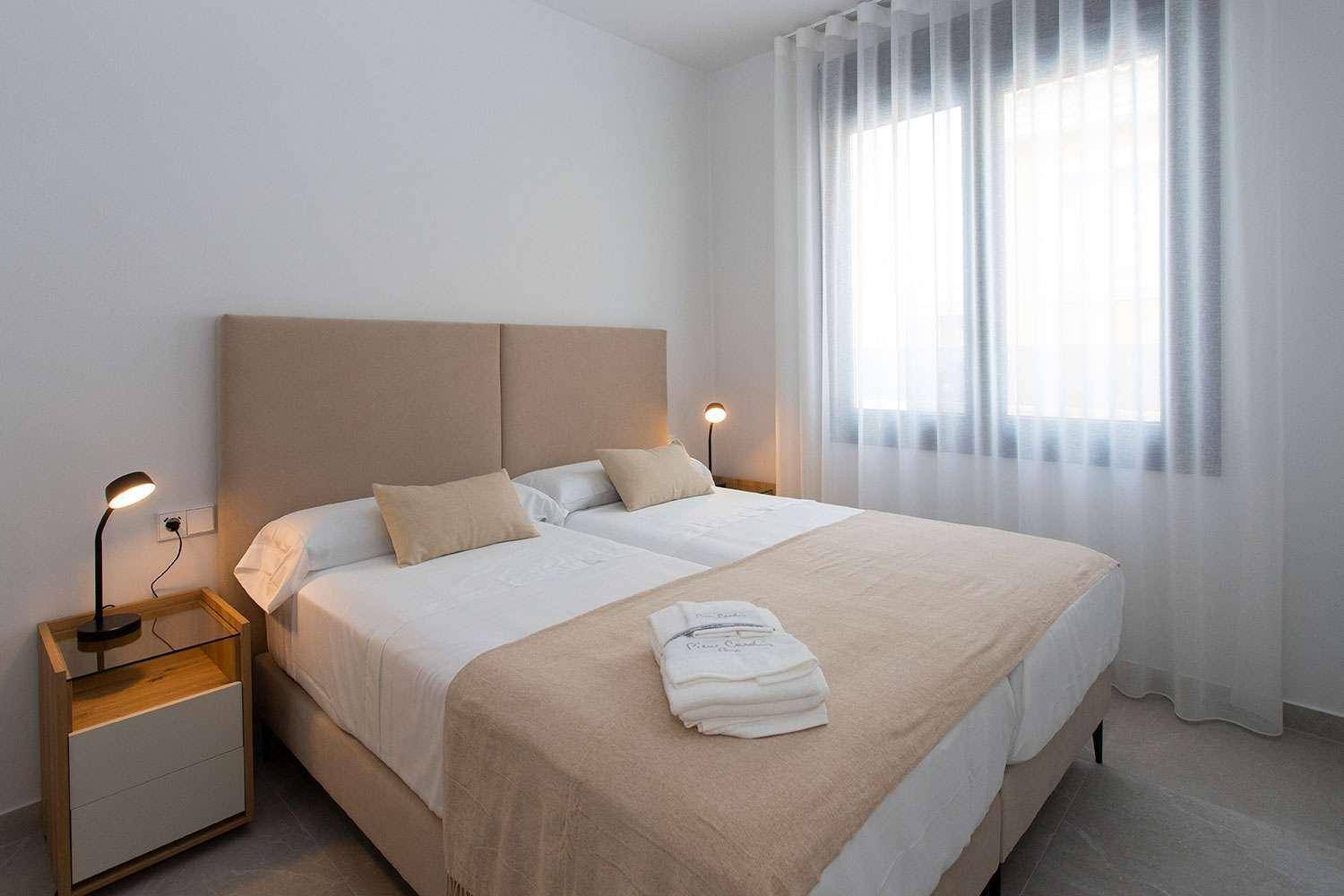 Helles Schlafzimmer mit zwei Einzelbetten, Nachttischen und großen Fenstern für viel Tageslicht.