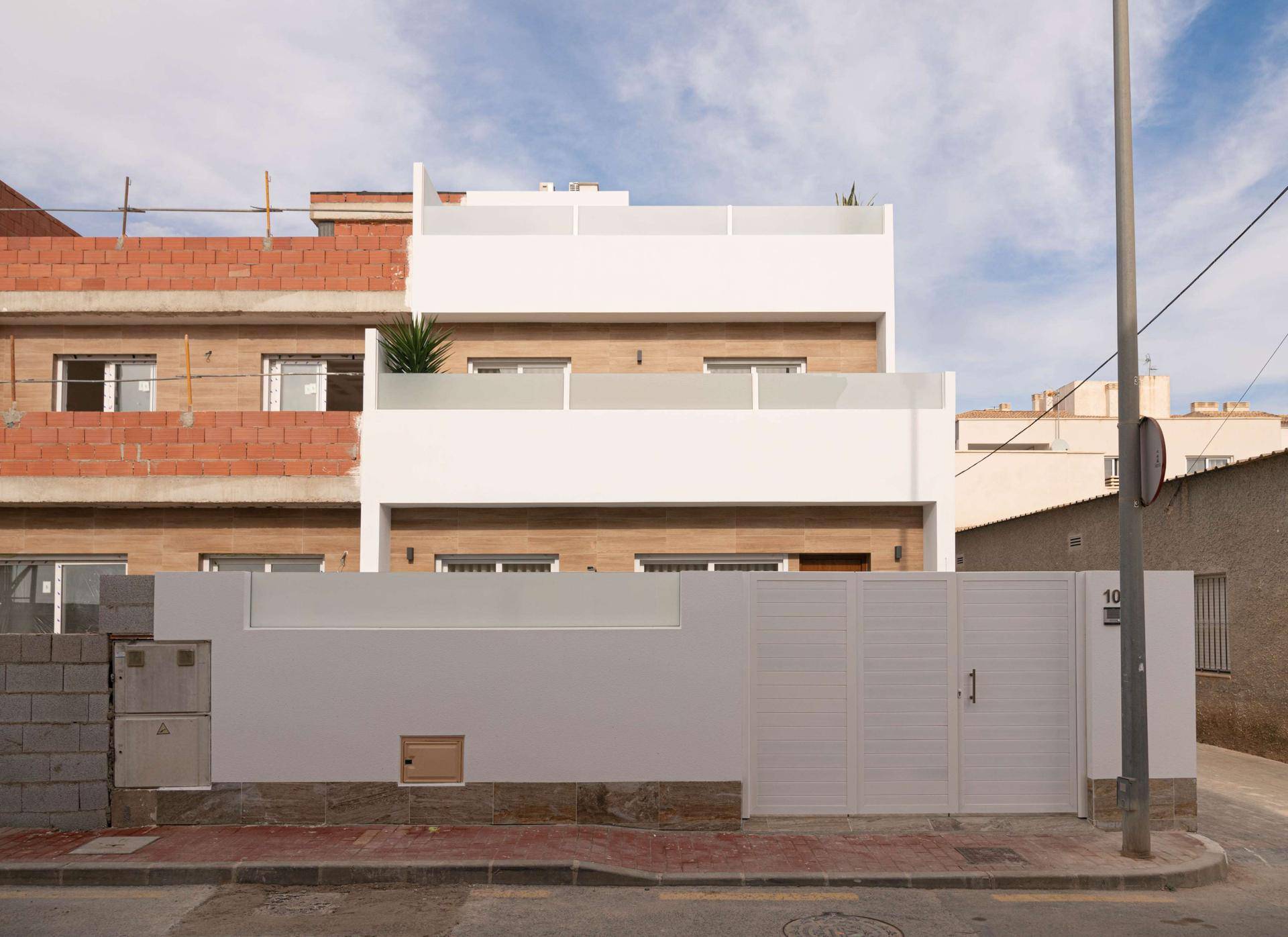 Moderne Hausfassade mit weißem Anstrich und Holzverkleidung, umgeben von einer Wohnstraße.