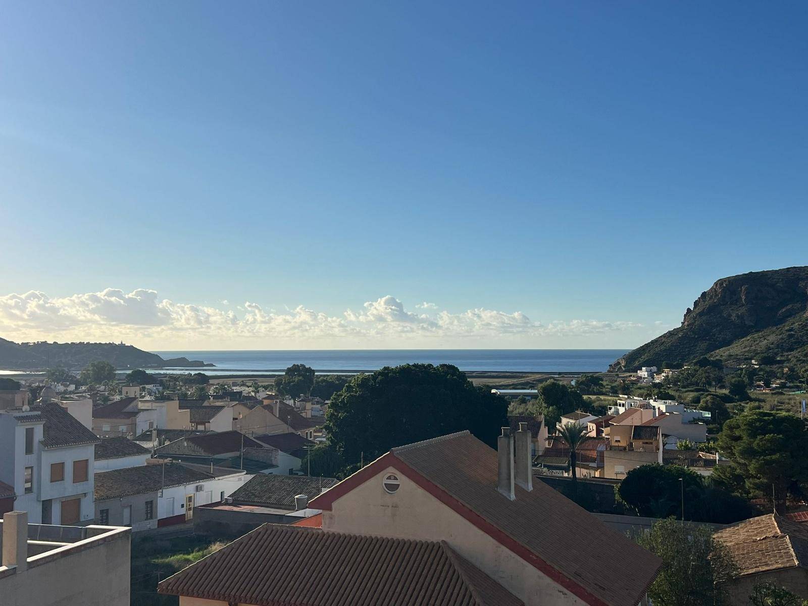 Sonniger Ausblick über die Dächer einer Küstenstadt zum blauen Meer und den Bergen im Hintergrund.