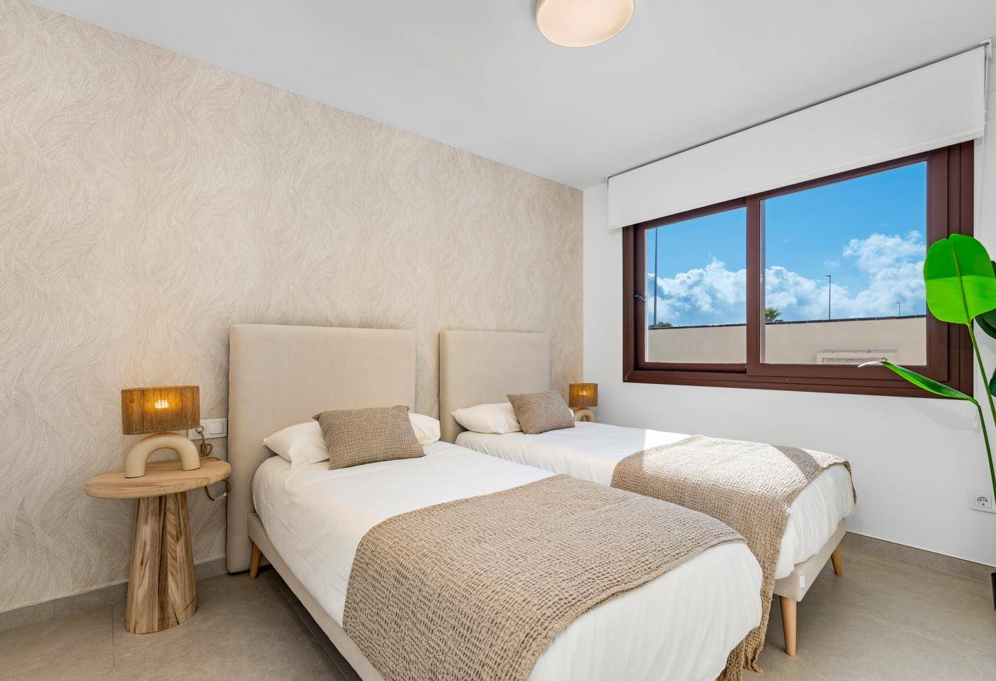 Modernes Schlafzimmer mit zwei Einzelbetten, beiger Wand und großem Fenster für viel Tageslicht.