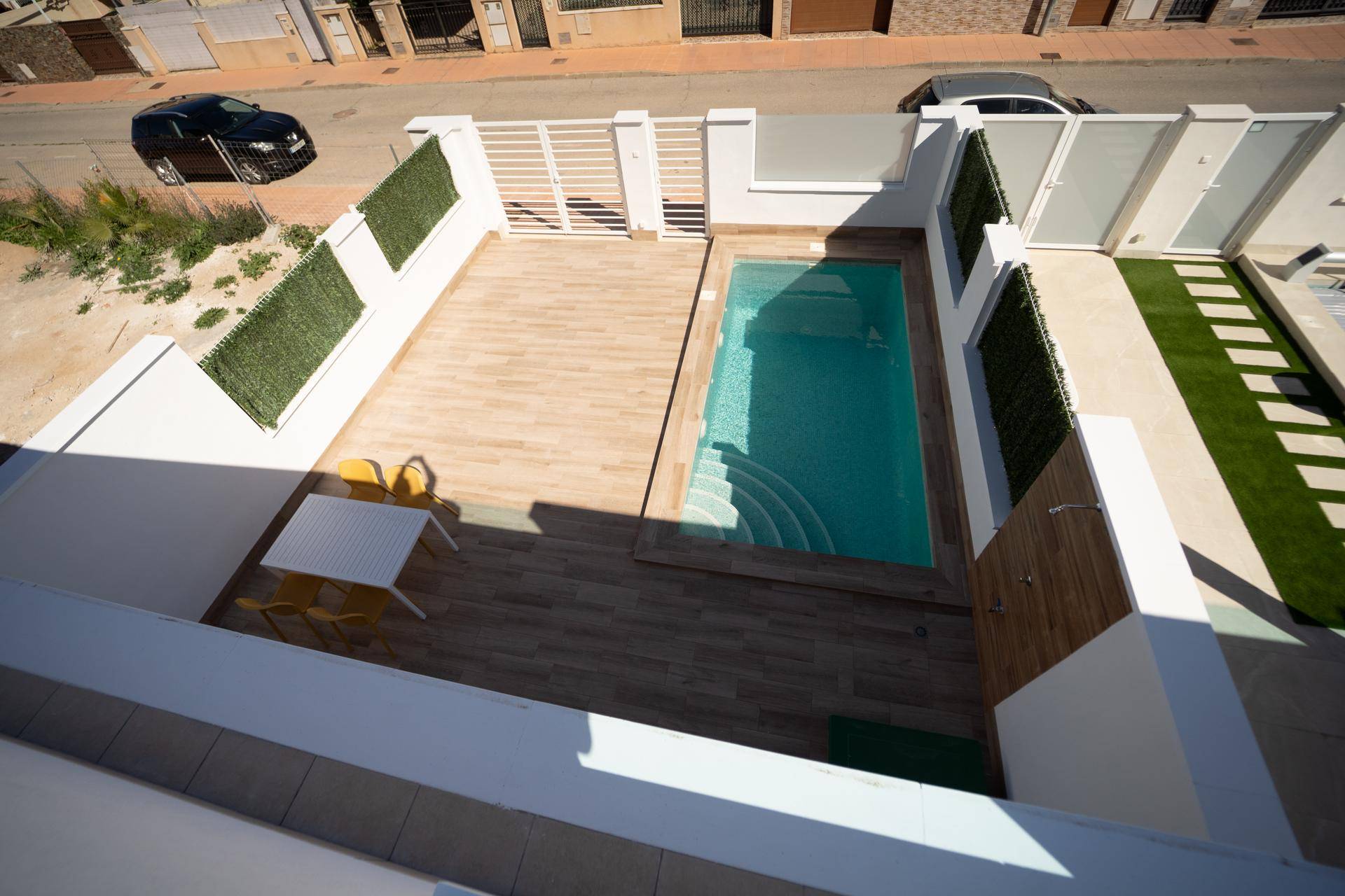 Privater Außenbereich mit Pool, Holzterrasse und Kunstrasenstreifen in sonniger Lage.