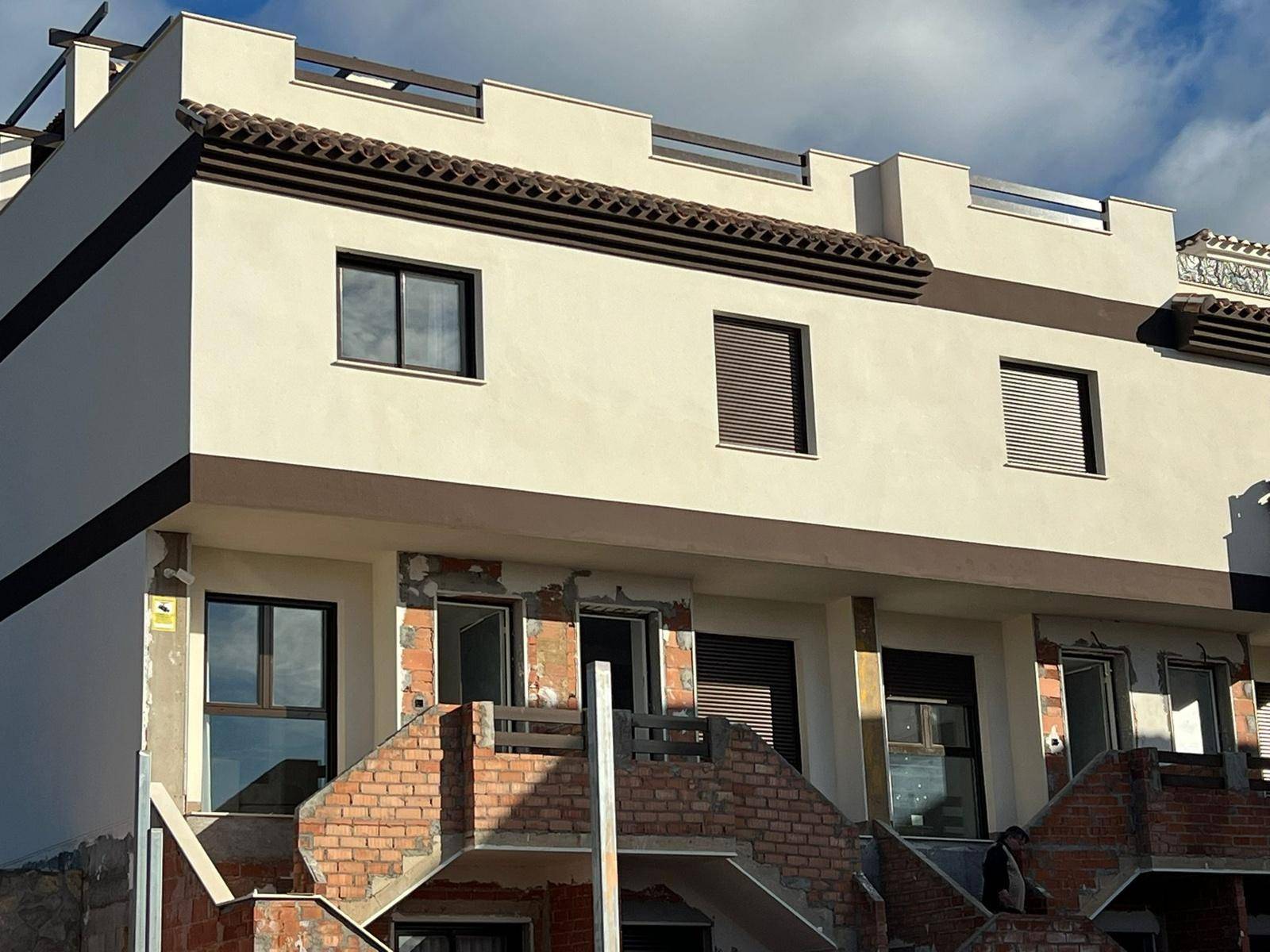 Fassade eines im Bau befindlichen Reihenhauses mit sichtbaren Ziegeln und Fenstern.