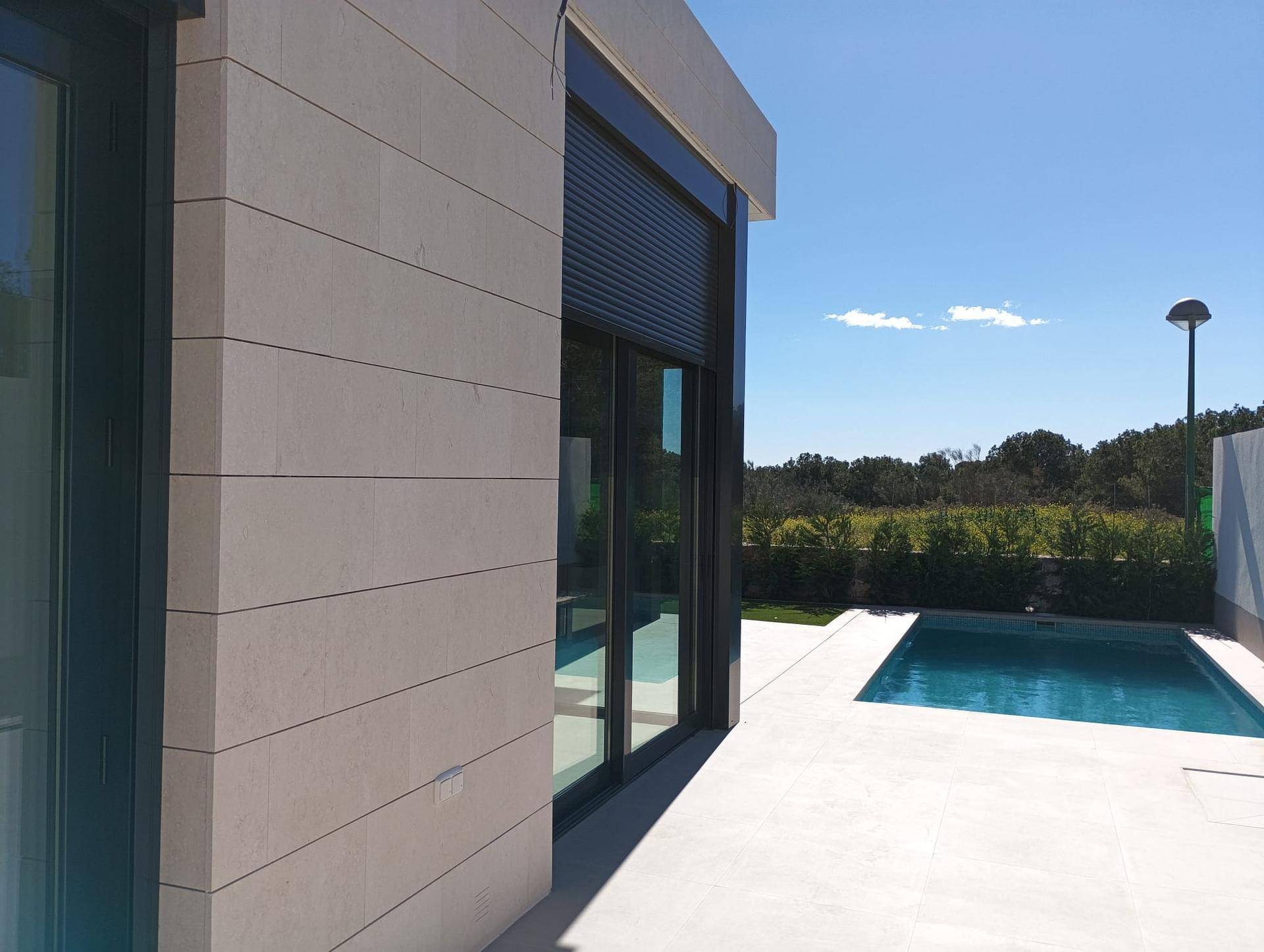 Moderne Hausfassade mit großen Schiebefenstern und Blick auf den angrenzenden Poolbereich.