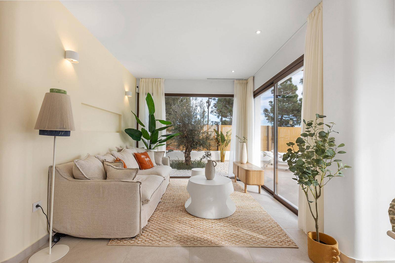 Gemütliches Wohnzimmer mit hellem Sofa, modernen Beistelltischen und großen Fenstern.