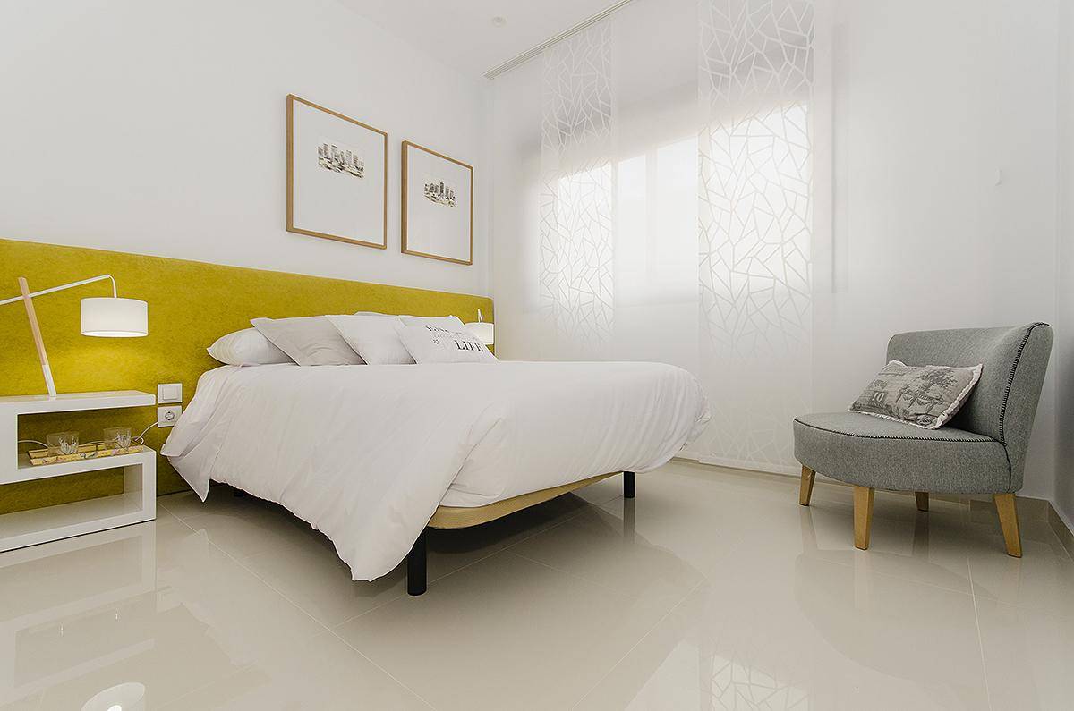 Helles Schlafzimmer mit modernem Bett, gelbem Kopfteil und großen Fenstern.