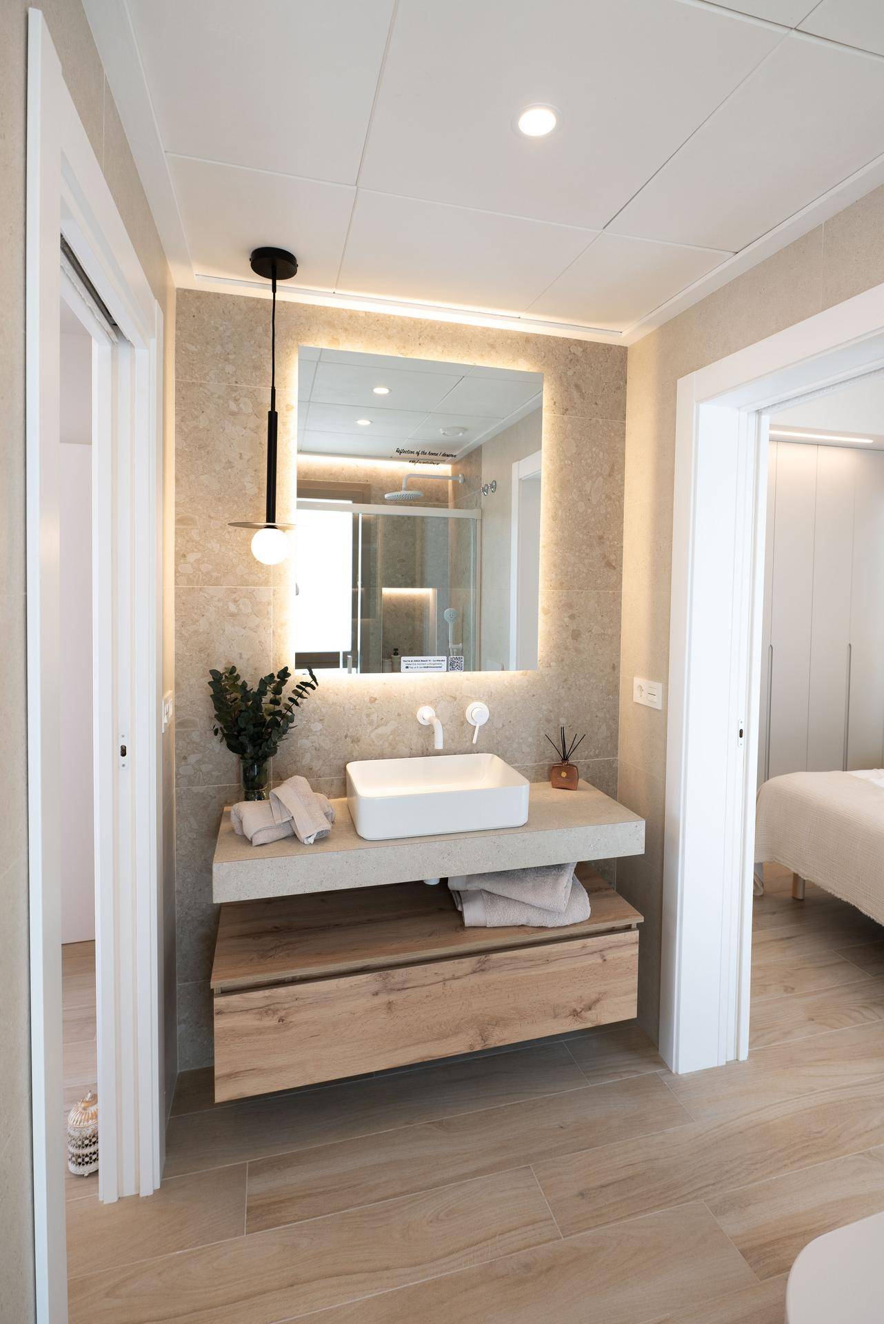 Modernes Badezimmer mit Einzelwaschbecken, beleuchtetem Spiegel und Zugang zum Schlafzimmer.