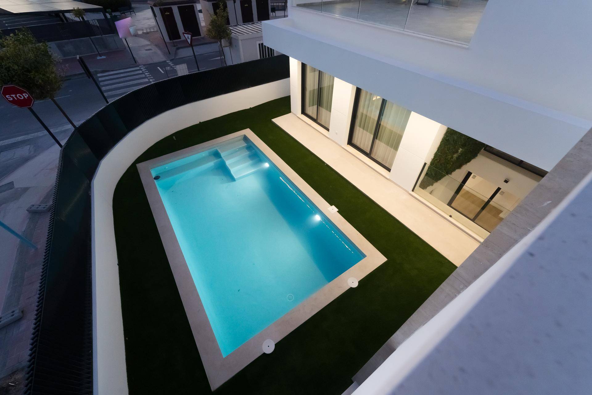 Beleuchteter Poolbereich mit Kunstrasen und moderner Architektur von oben bei Nacht.