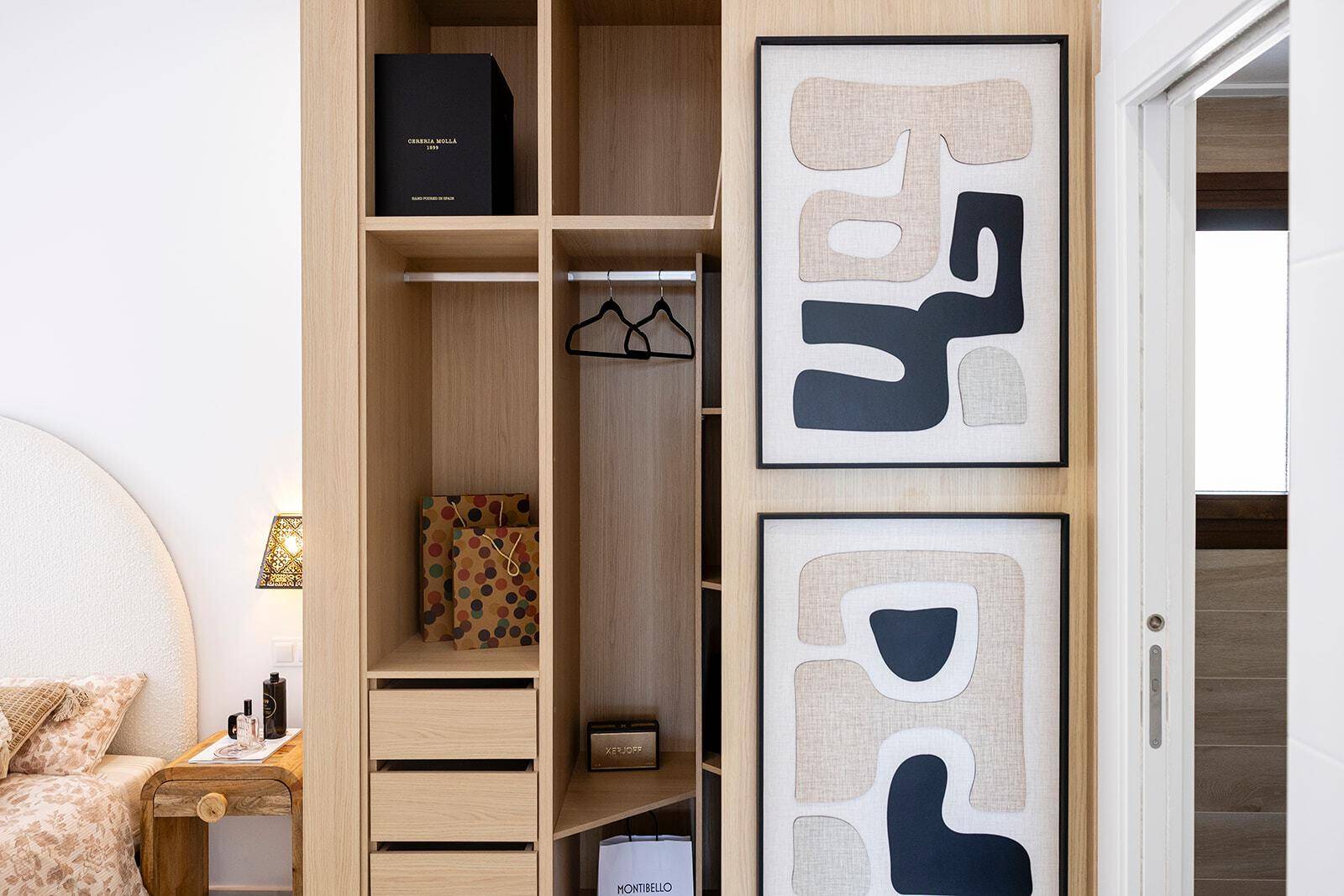 Offener Kleiderschrank im Schlafzimmer mit Regalen, Schubladen und moderner Kunst.