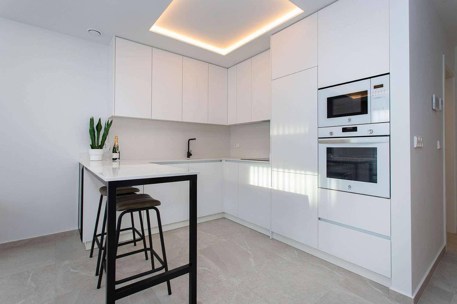 Moderne weiße Küche mit integrierten Geräten, Kochinsel und indirekter Deckenbeleuchtung für Ambiente.