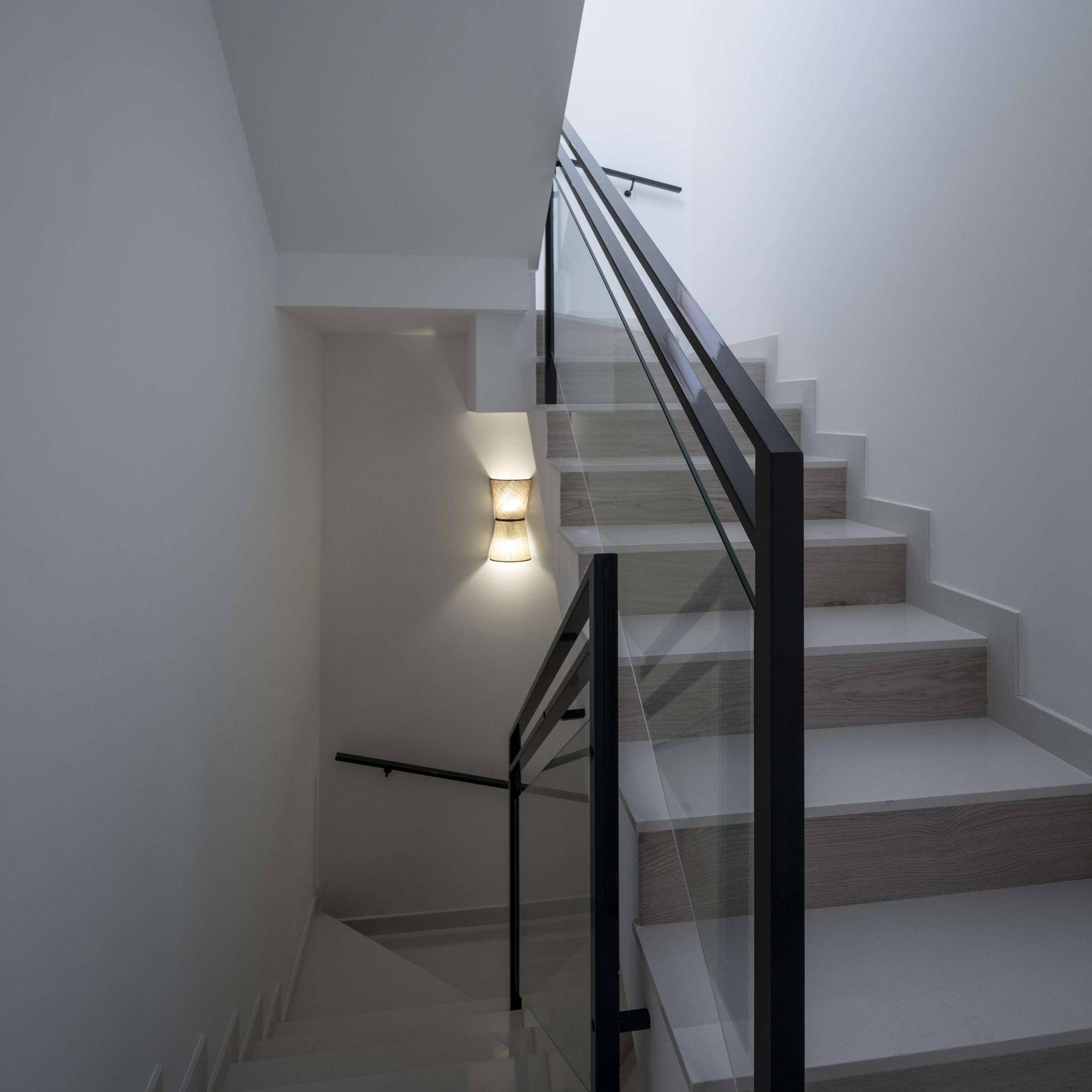 Elegante Treppe mit Glasgeländer und Wandleuchte, die die oberen Etagen erschließt.
