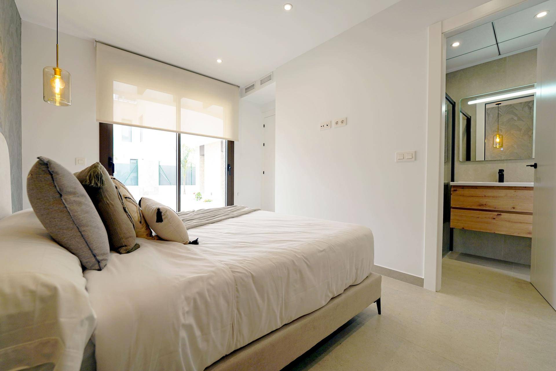 Helles Schlafzimmer mit großem Bett, Fenster und direktem Zugang zu einem modernen Badezimmer.
