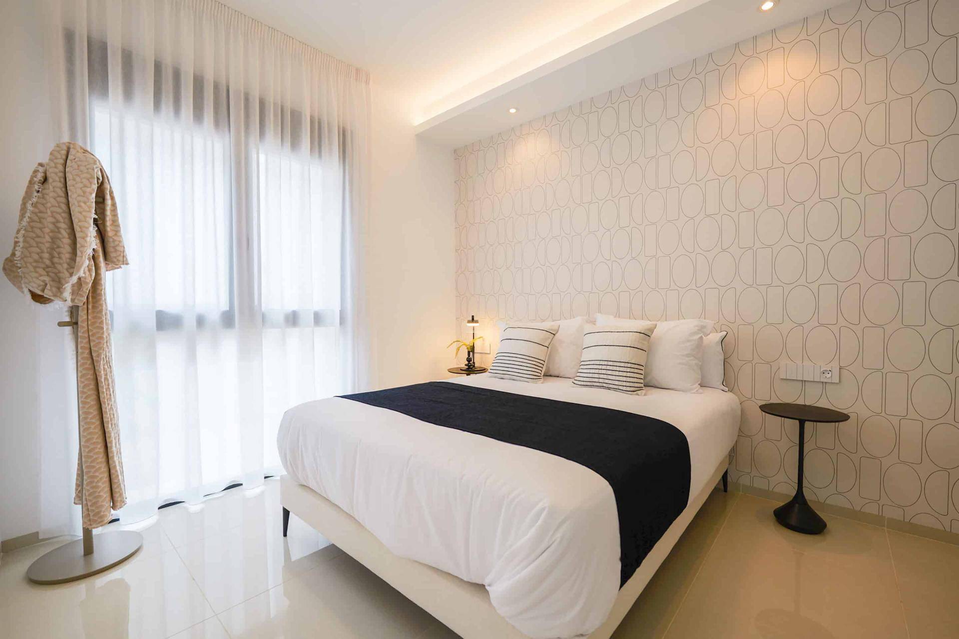 Helles Schlafzimmer mit grafischer Tapete, großem Fenster und minimalistischer Einrichtung.