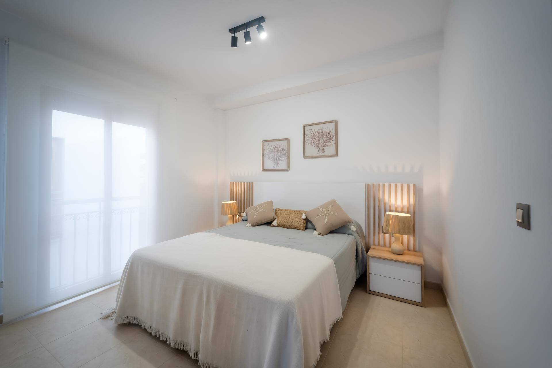 Helles Schlafzimmer mit Doppelbett, Nachttischen und Zugang zu einem französischen Balkon.
