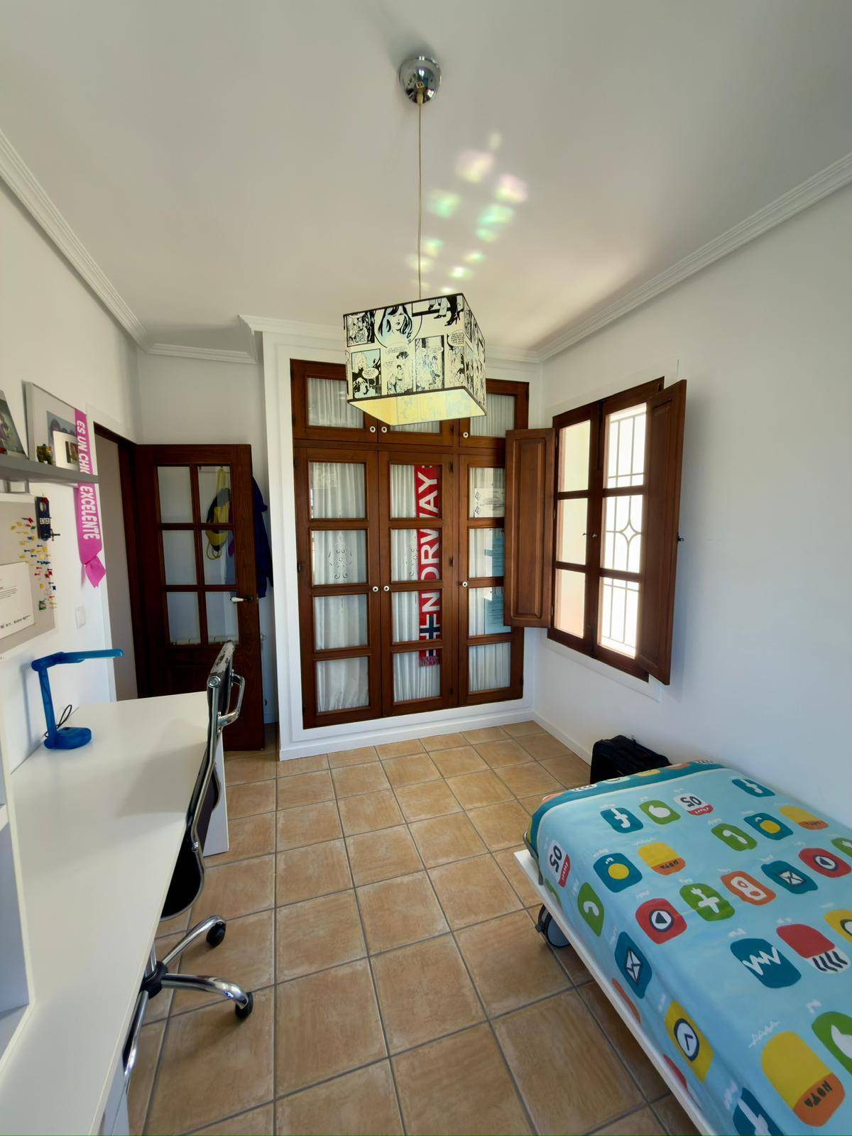 Helles Schlafzimmer mit Einzelbett, Schreibtisch und traditionellen Holzfenstern.