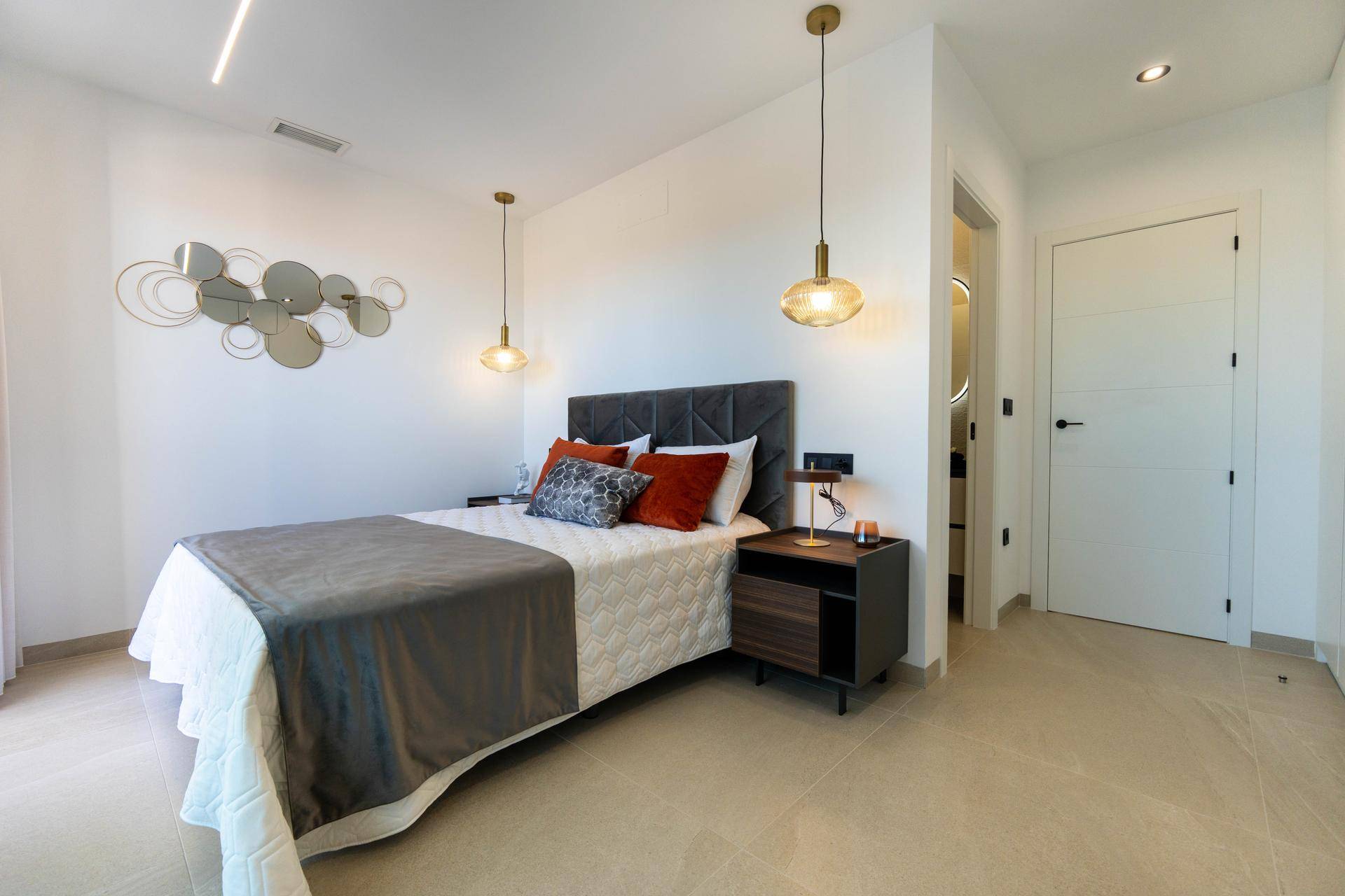 Helles Schlafzimmer mit modernem Bett, Nachttischen und Zugang zu einem angrenzenden Bad.