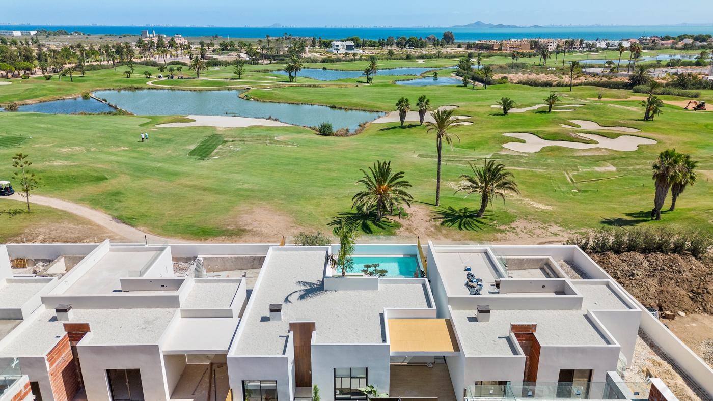 Luftaufnahme einer modernen Wohnanlage mit Pools und Golfplatz in Küstennähe.