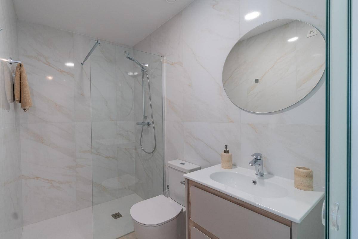 Elegantes Badezimmer mit Marmoroptik-Fliesen, moderner Dusche und Waschtisch mit rundem Spiegel.