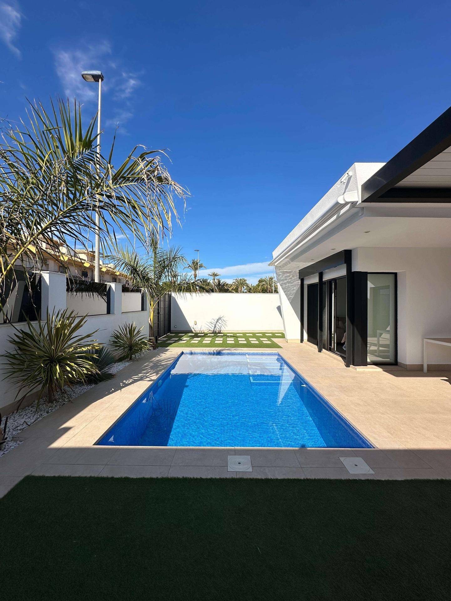 Langer, rechteckiger Pool im Gartenbereich der modernen Villa unter strahlend blauem Himmel.