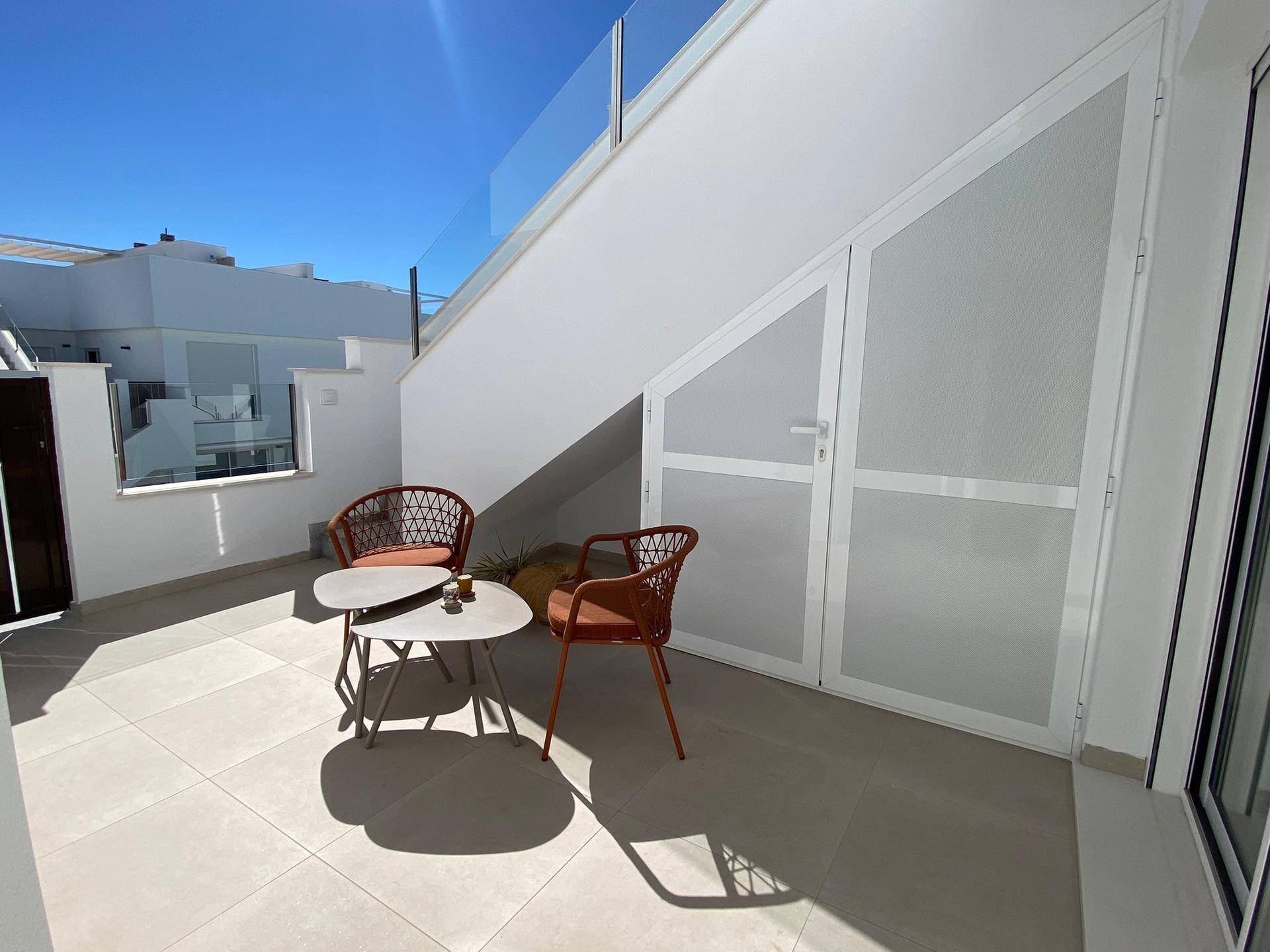 Kleine, geflieste Terrasse mit Sitzgelegenheiten unter einer Treppe.