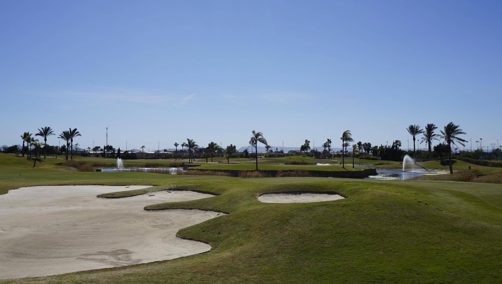 Golfplatz mit Sandbunkern, Wasserhindernissen und Palmen unter klarem Himmel.