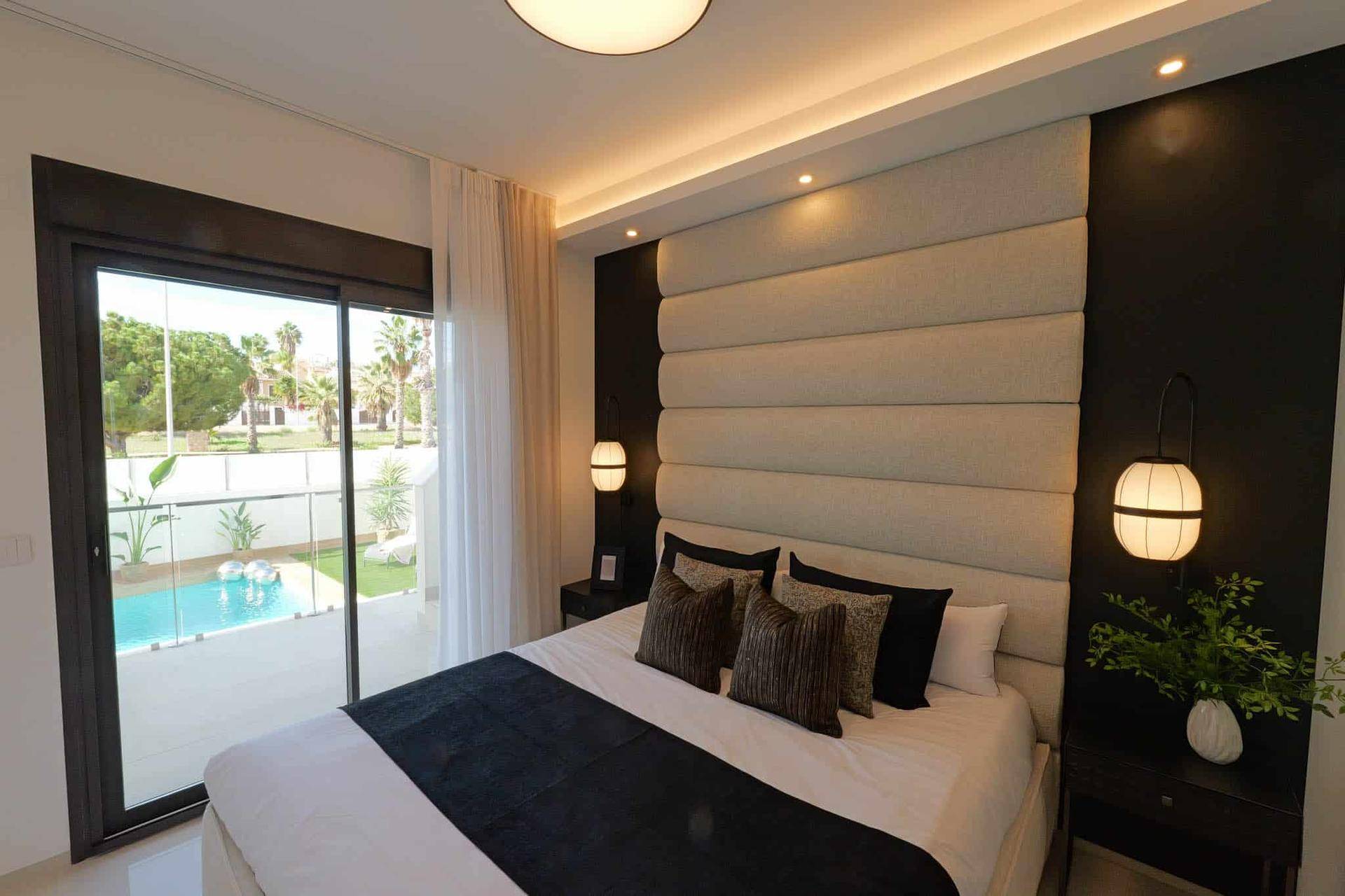 Modernes Schlafzimmer mit großem Bett, gepolstertem Kopfteil und Schiebetür zum Poolbereich.
