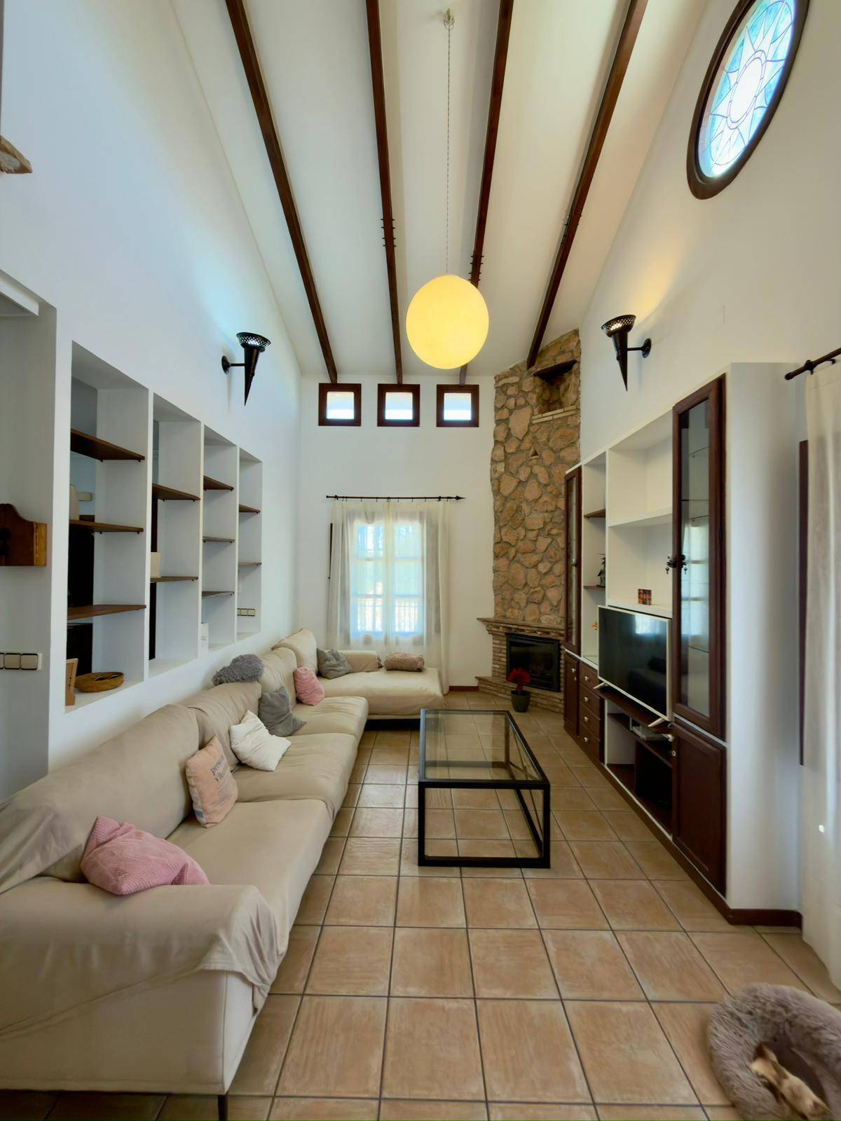 Helles Wohnzimmer mit bequemer Couch, hohen Decken und traditionellem Steinkamin.