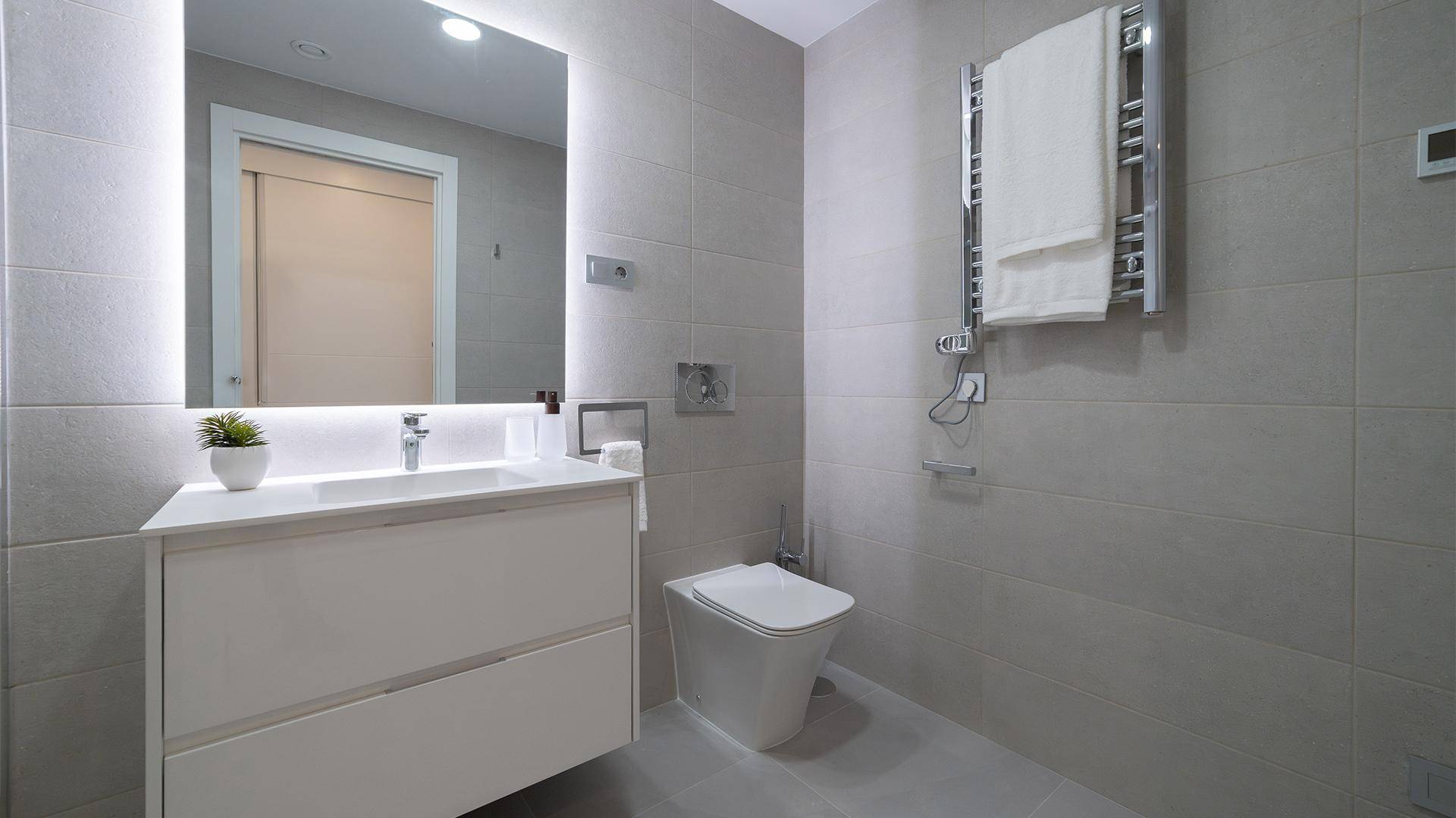 Modernes Badezimmer mit Waschtisch, beleuchtetem Spiegel und Wand-WC.