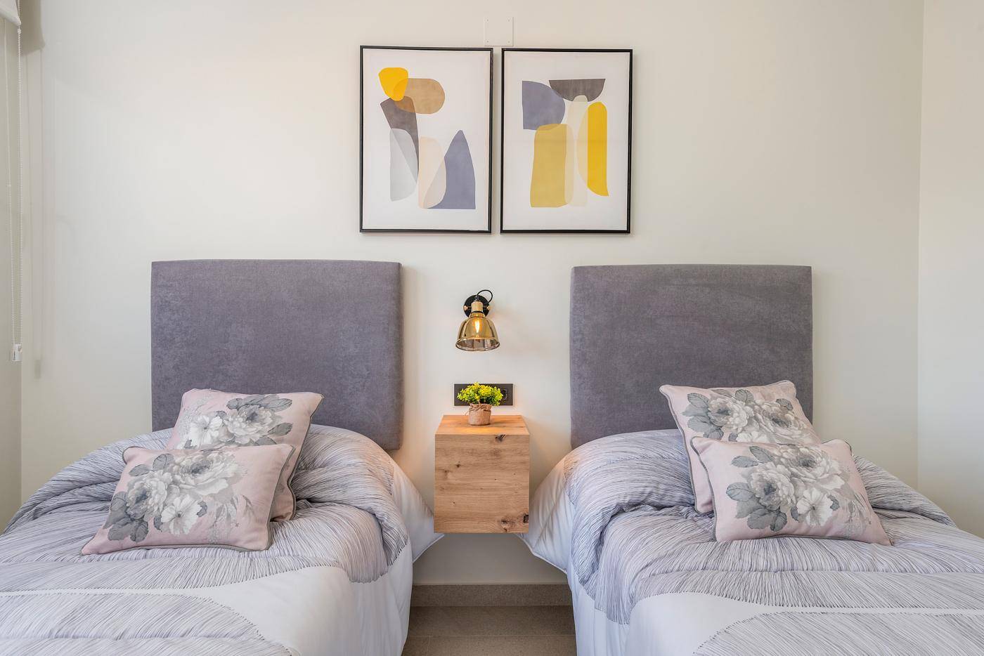 Schlafzimmer mit zwei Einzelbetten und modernen Kopfteilen, dekoriert mit abstrakten Bildern.
