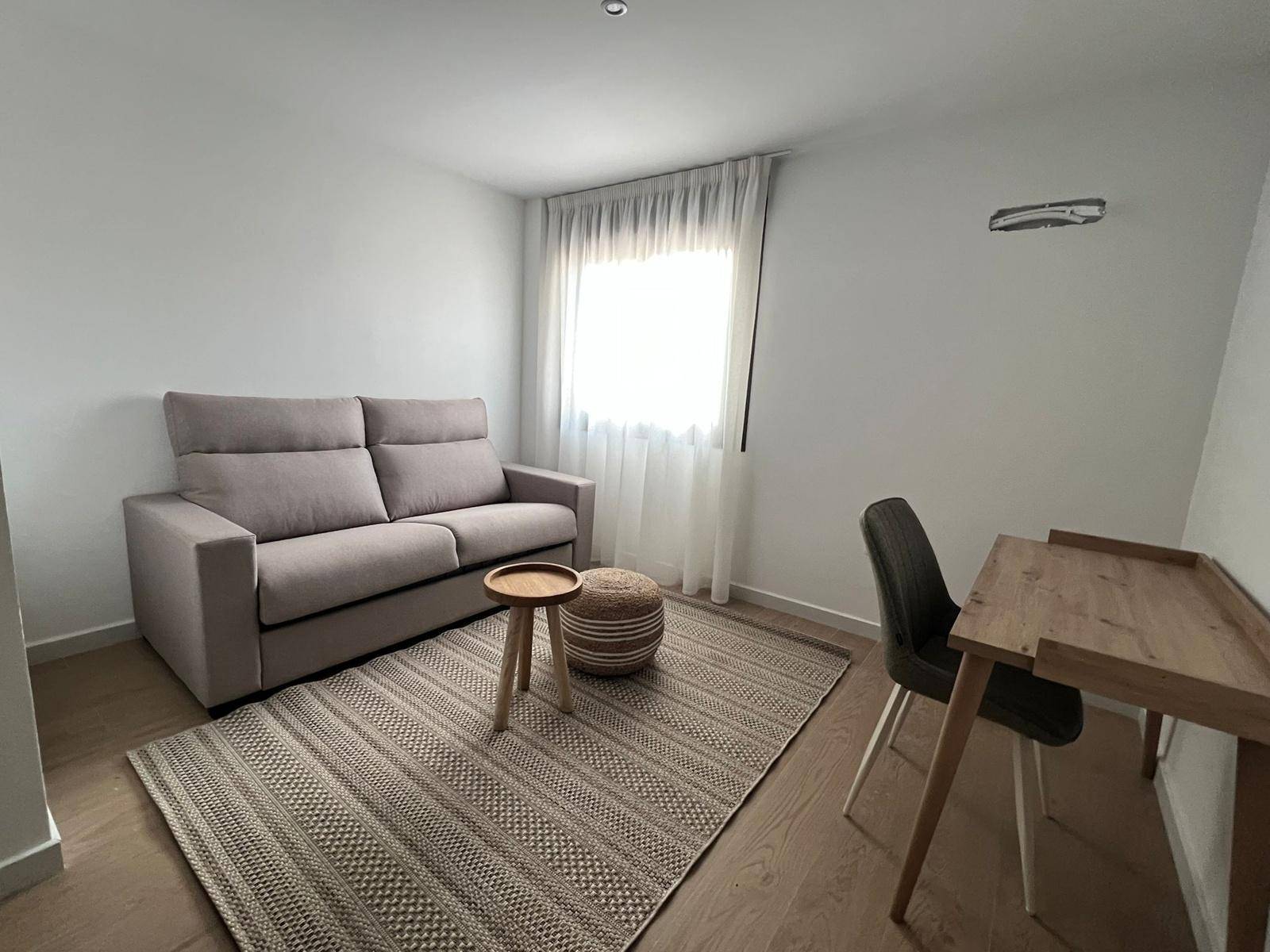 Funktionales Arbeitszimmer mit Schlafsofa, Holztisch und natürlichem Lichteinfall.