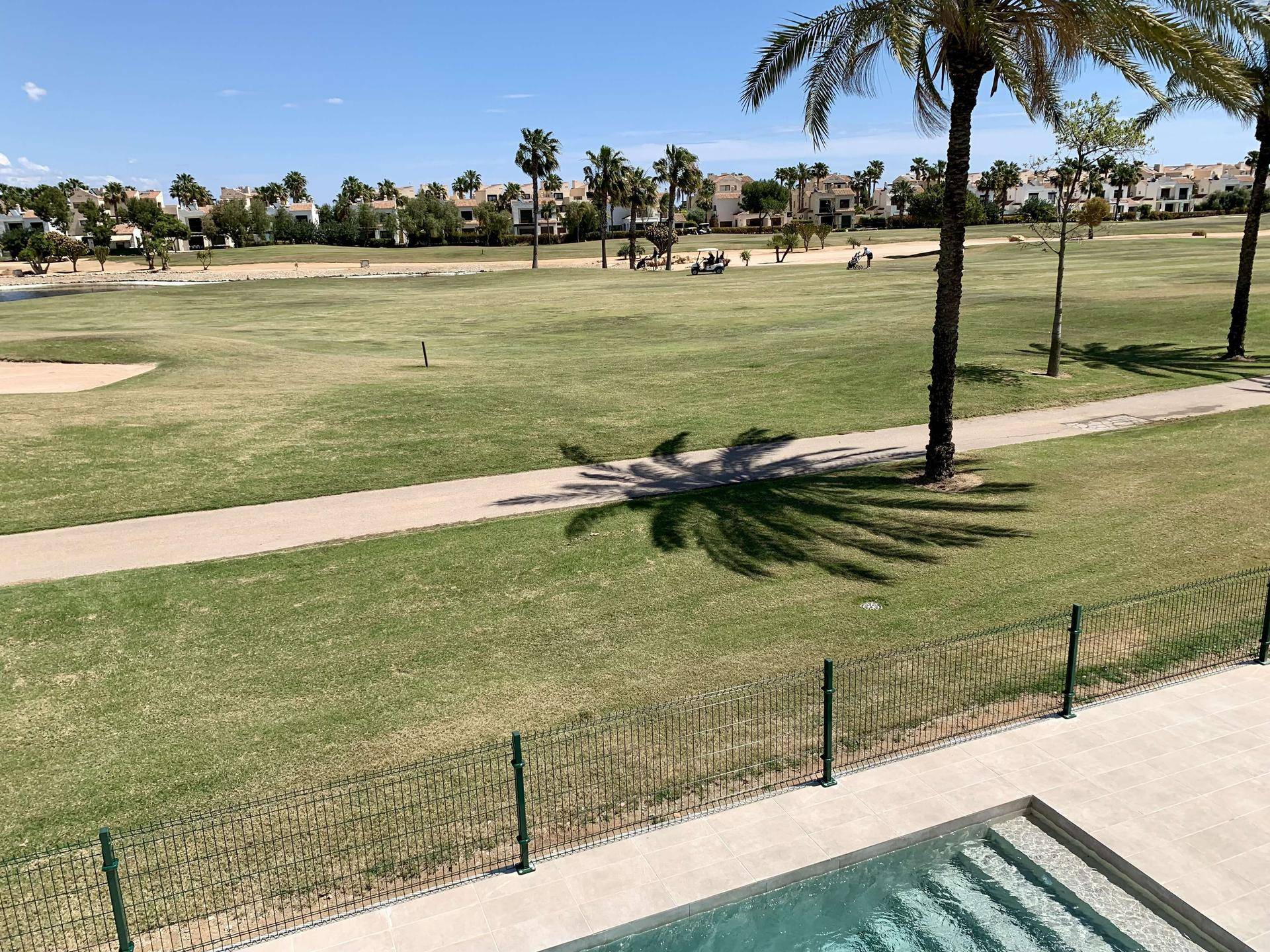 Weitläufiger Golfplatz mit Palmen und einem Pool im Vordergrund unter blauem Himmel.