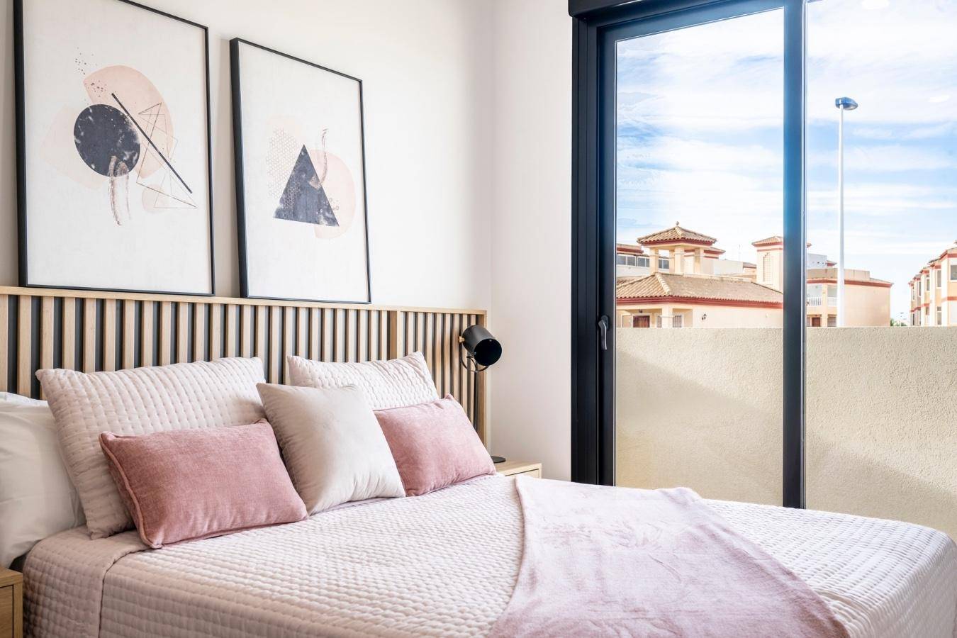 Helles Schlafzimmer mit Doppelbett, modernen Bildern und großem Fenster mit Blick auf die Nachbarschaft.