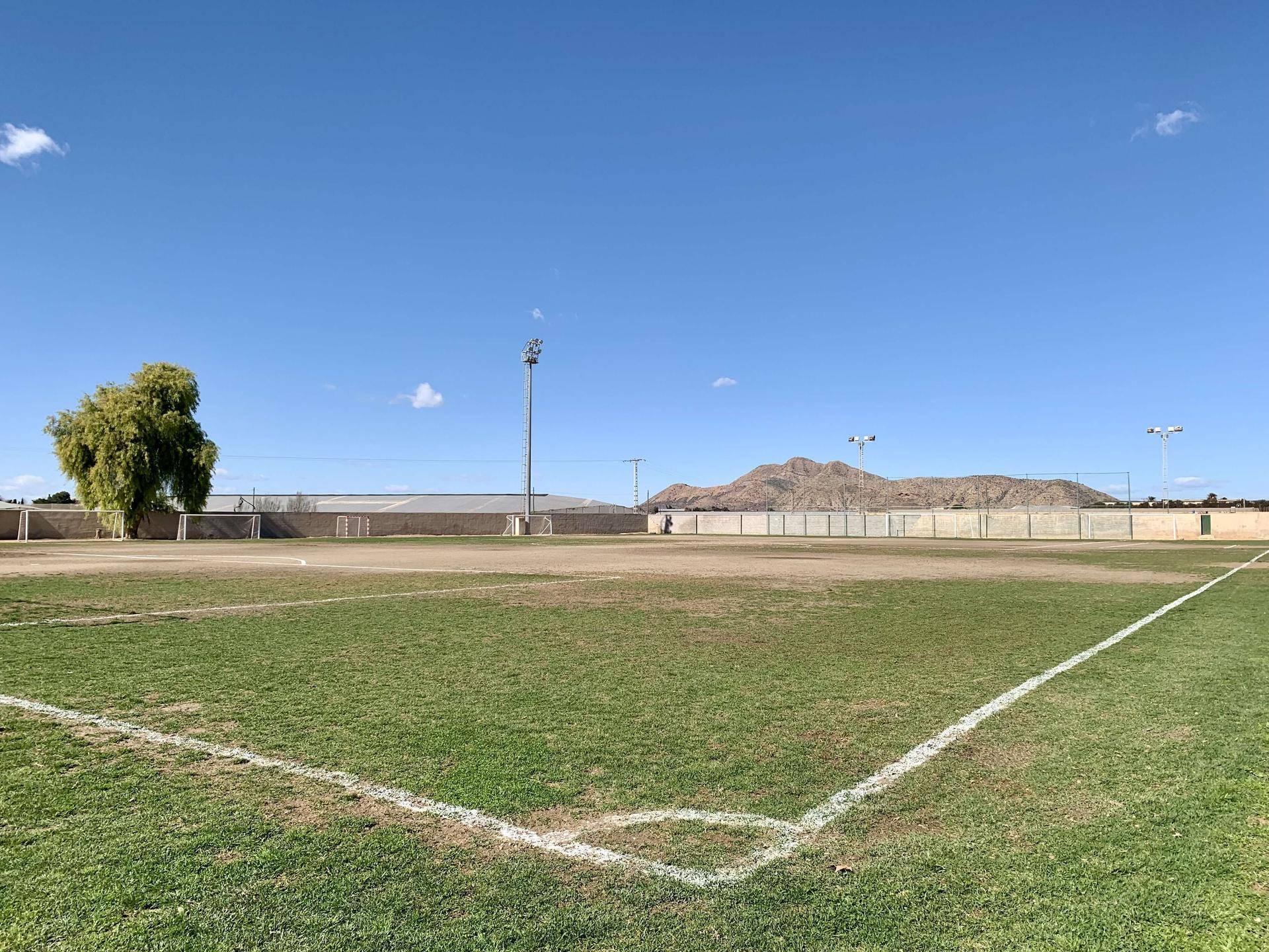 Grüner Sportplatz mit Bergen im Hintergrund unter klarem, blauem Himmel.