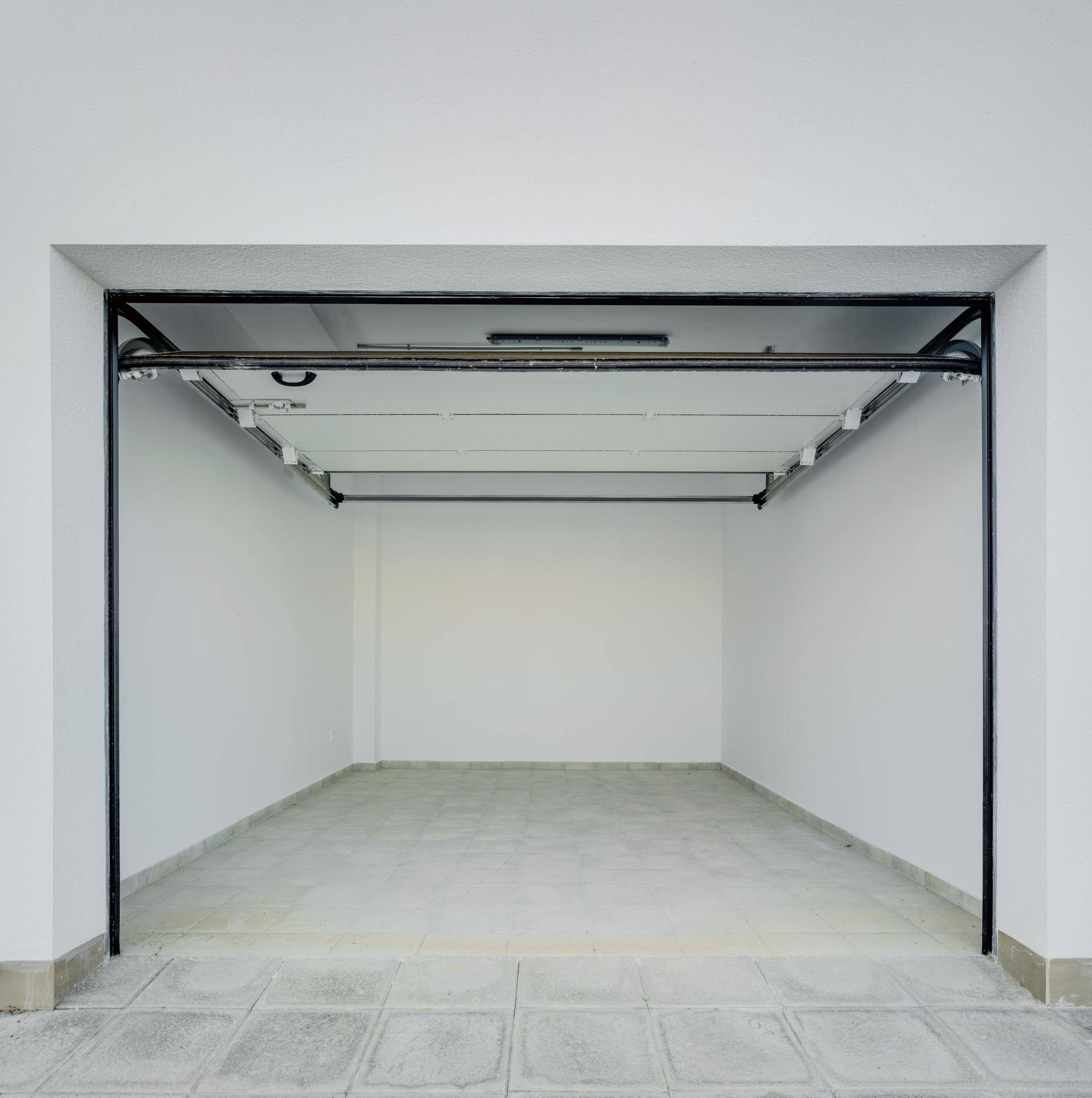 Leere Garage mit Fliesenboden und Rolltor, bereit zur Nutzung.