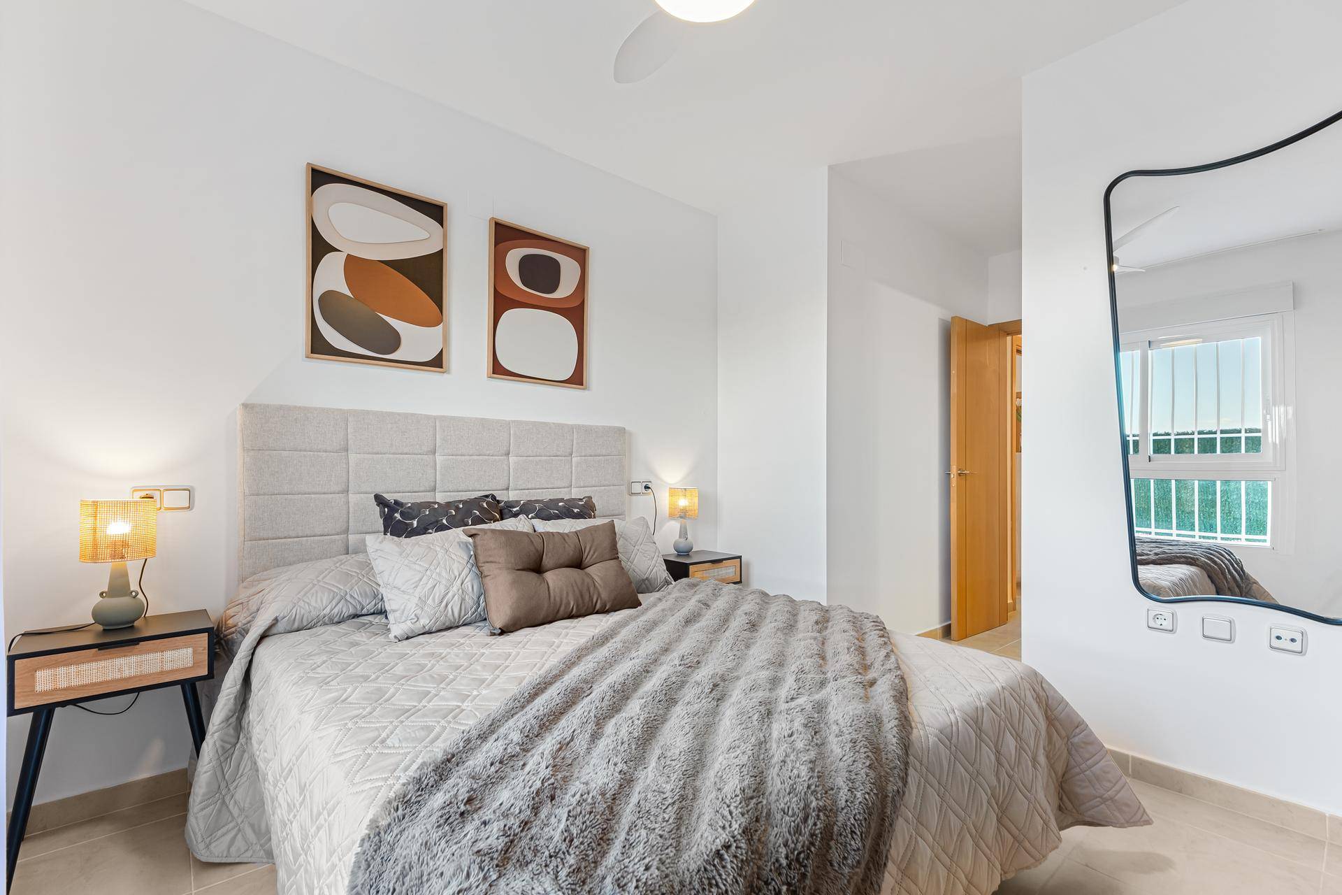 Schlafzimmer mit modernem Spiegel, Doppelbett und Zugang zu weiteren Räumen.