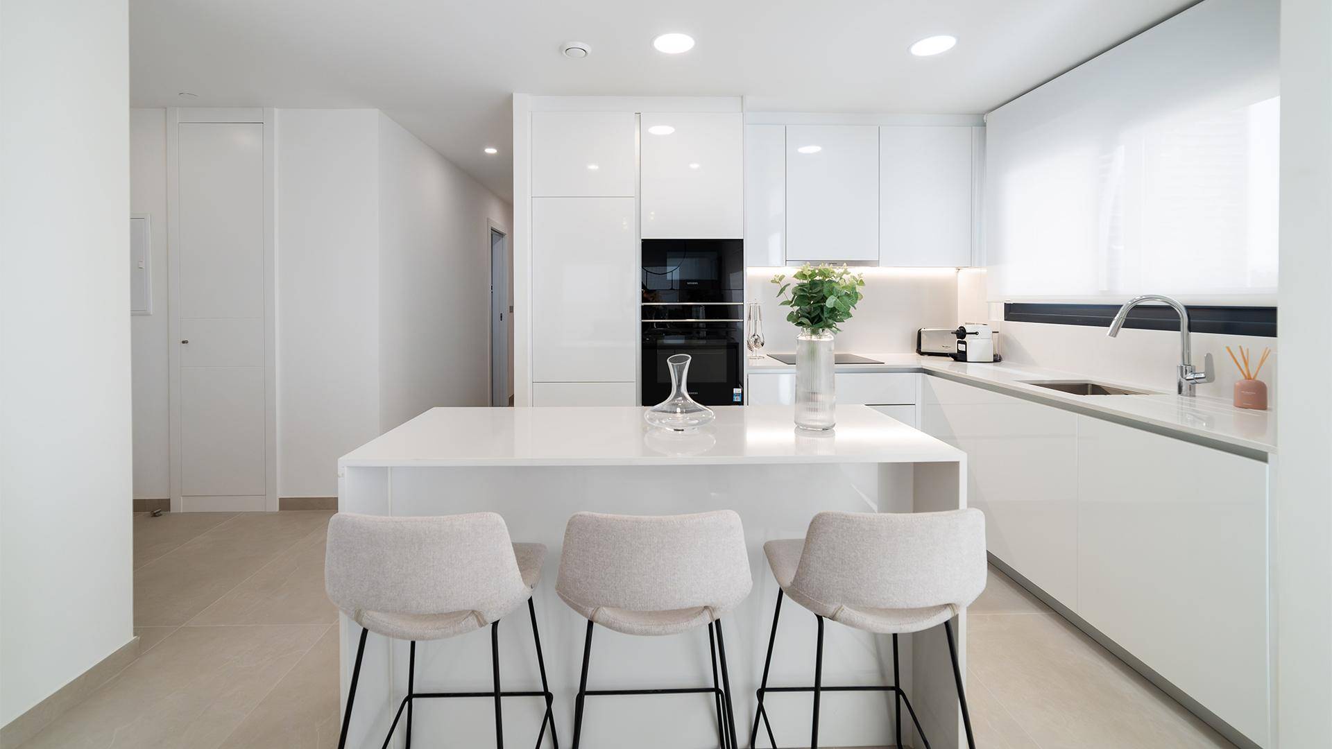 Moderne weiße Küche mit Kochinsel, integrierten Geräten und minimalistischem Design.
