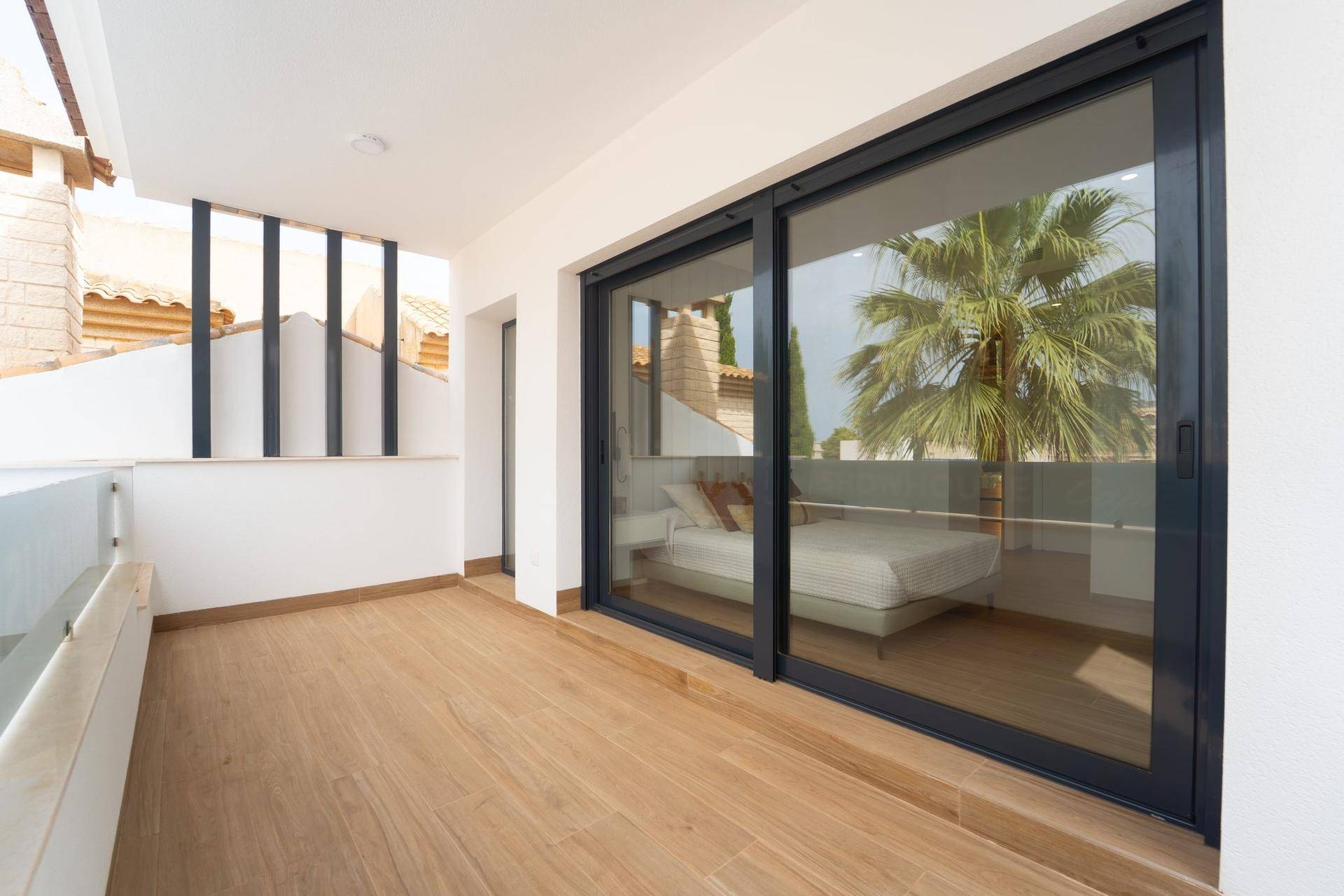 Heller Balkon mit Holzfliesen und Schiebetüren, die zu einem Schlafzimmer führen, mit Palmenblick.