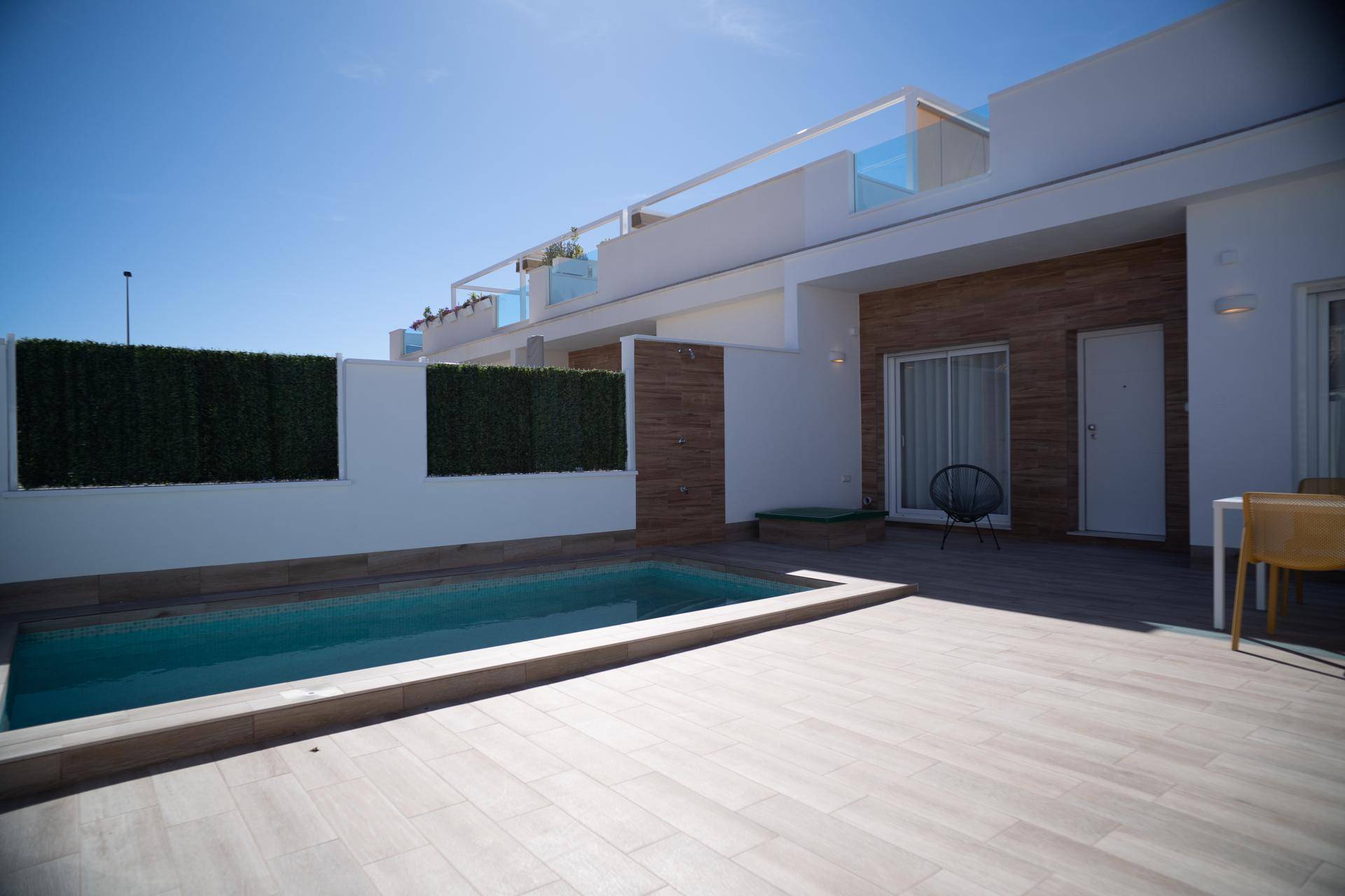 Vorderer Außenbereich mit Pool, Holzdeck und Sitzgelegenheiten vor einem modernen Haus.