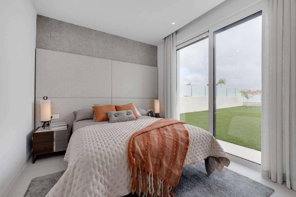 Modernes Schlafzimmer mit großem Bett, Nachttischen und bodentiefen Fenstern zum Garten.