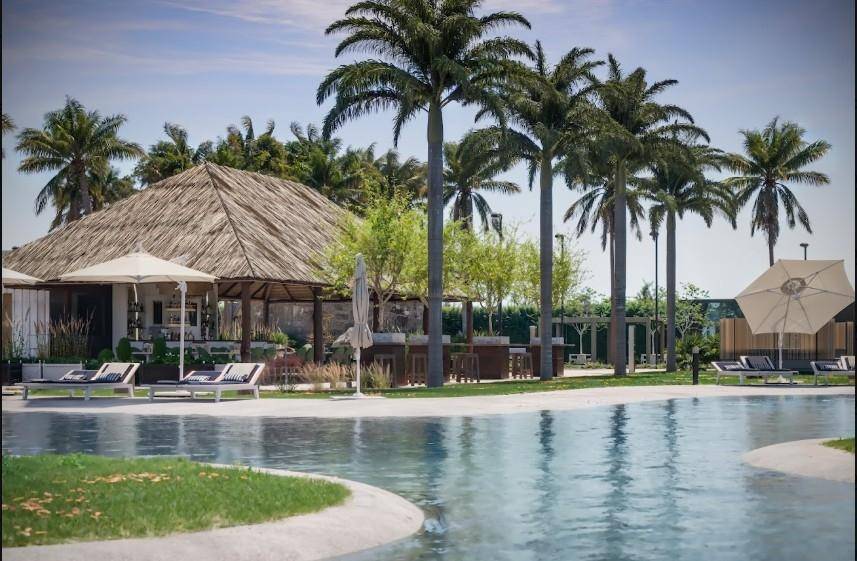 Großer Poolbereich mit Palmen, Liegestühlen und einem Restaurantgebäude mit Strohdach.