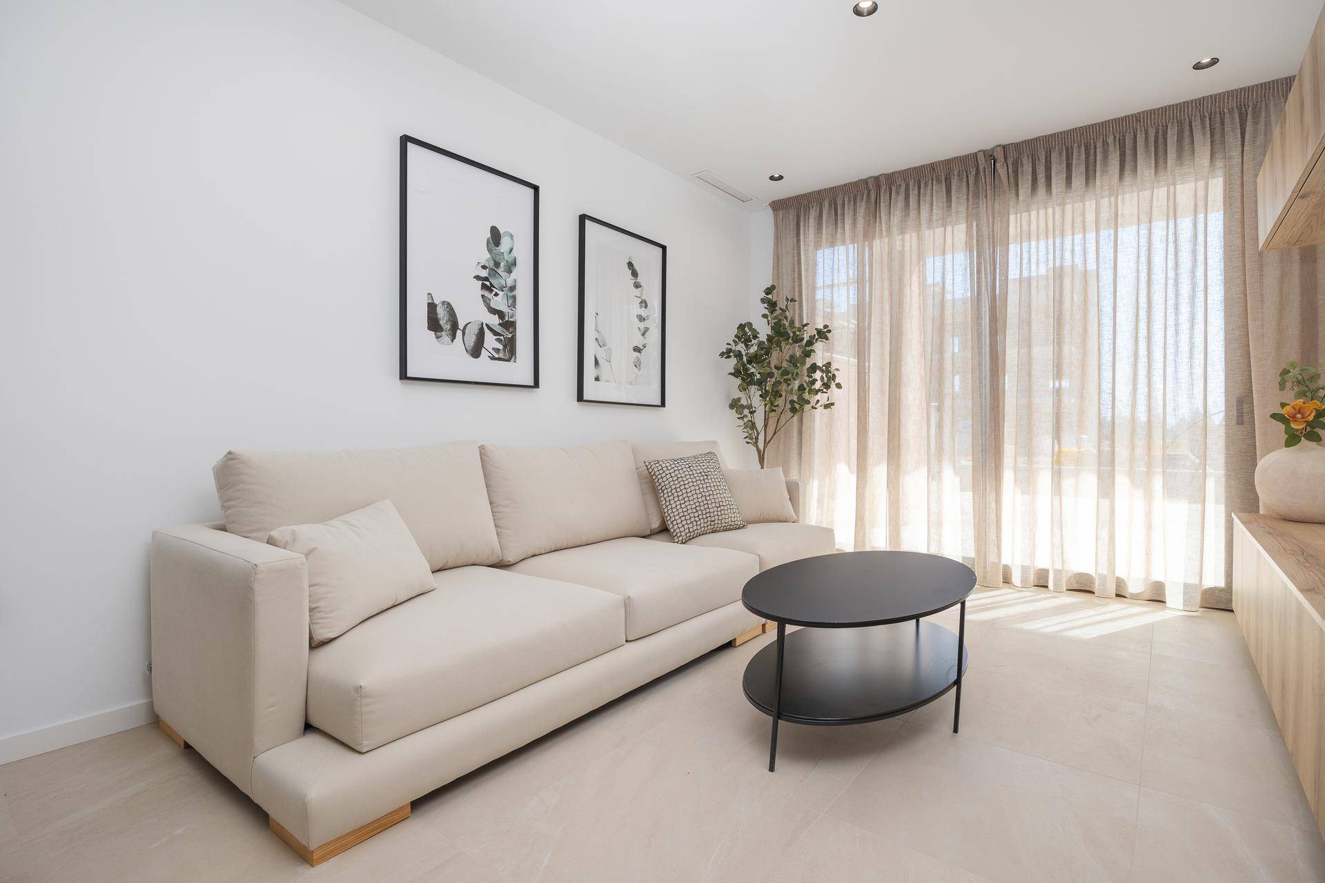 Gemütliches Wohnzimmer mit beigem Sofa, Couchtisch und großen Fenstern für viel Tageslicht.