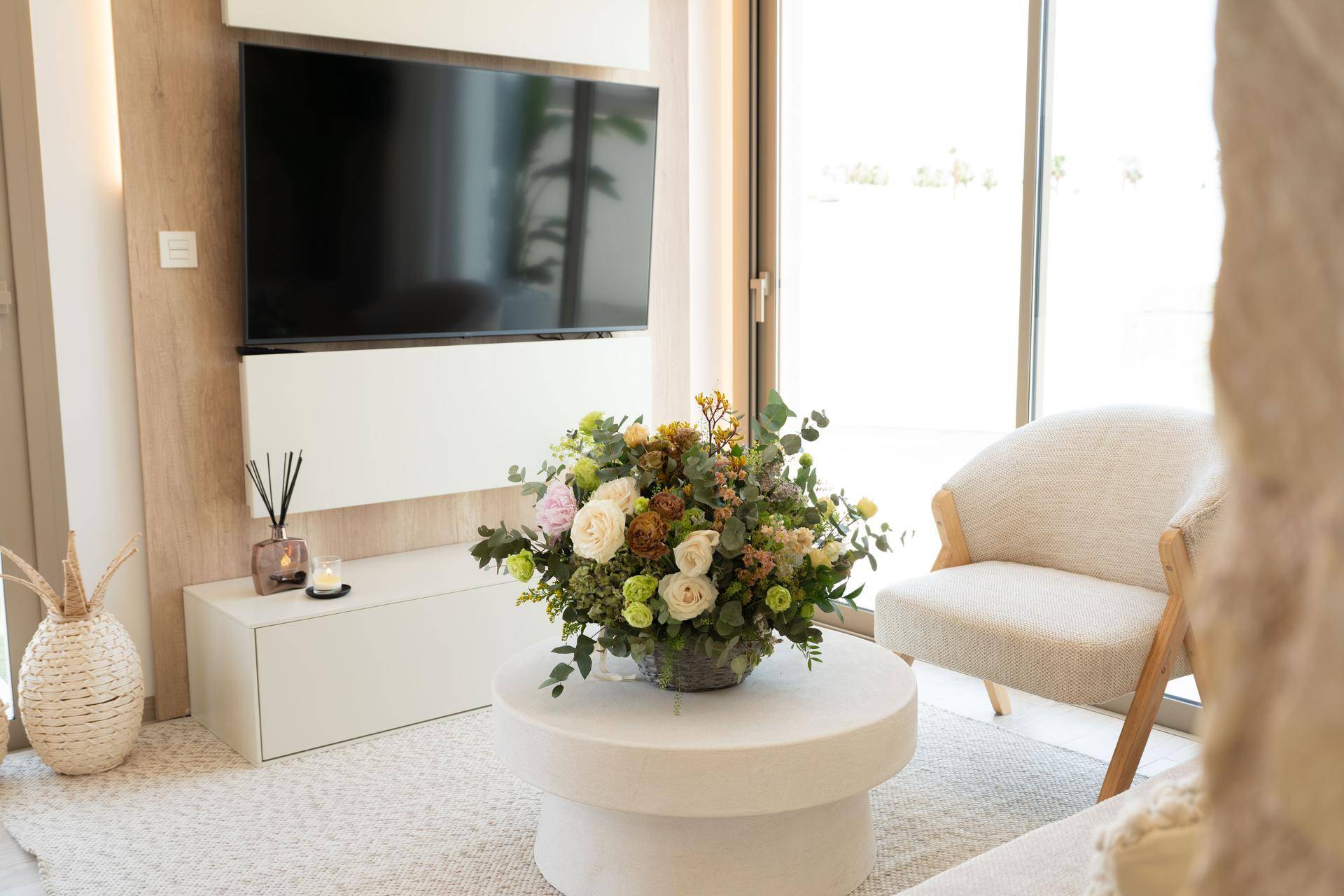 Detailansicht des Wohnzimmers mit modernem Couchtisch, Blumenarrangement und Fernseher.