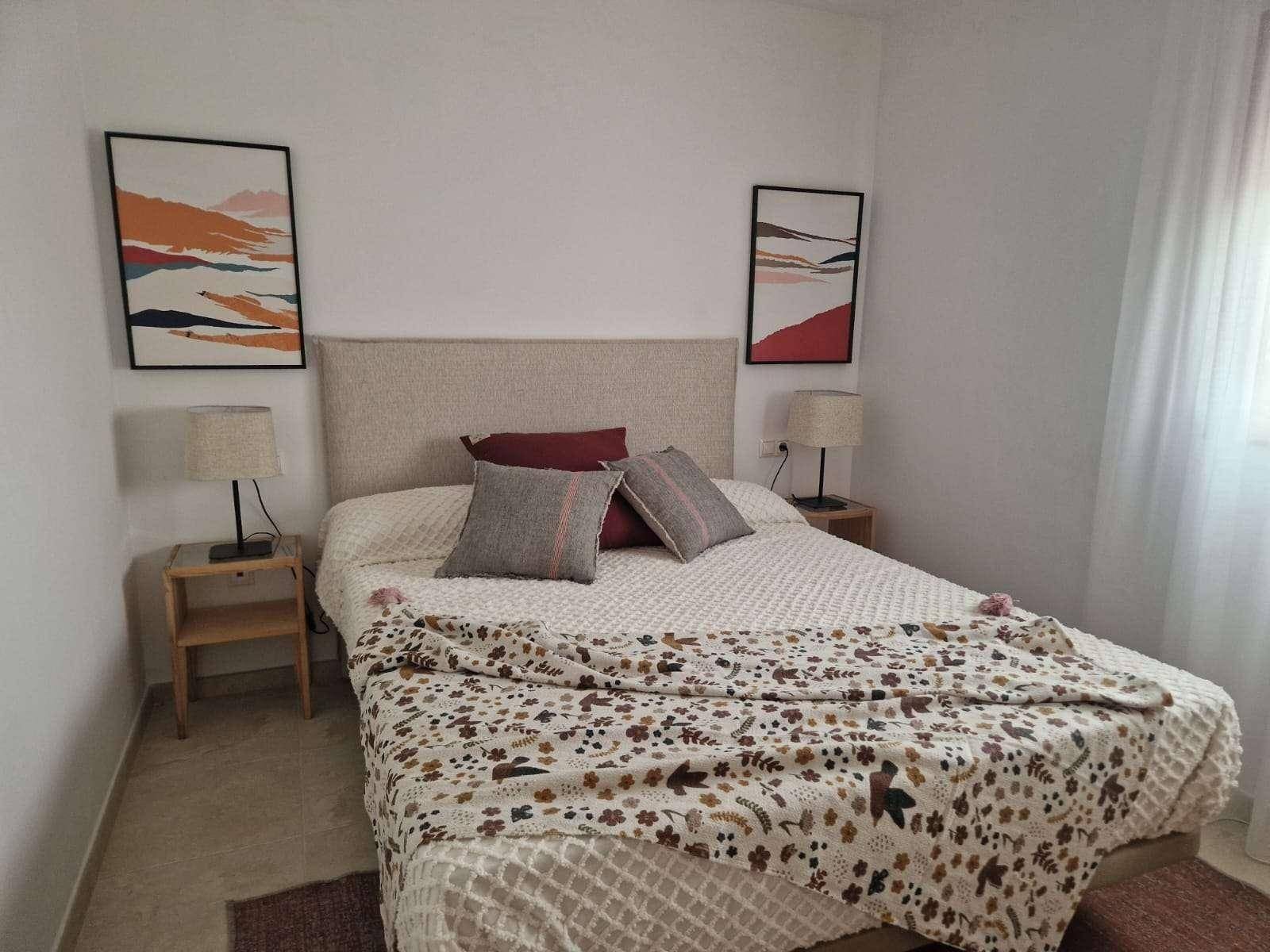 Schlafzimmer mit Doppelbett, beigem Kopfteil und zwei Nachttischen, dekoriert mit modernen Bildern.