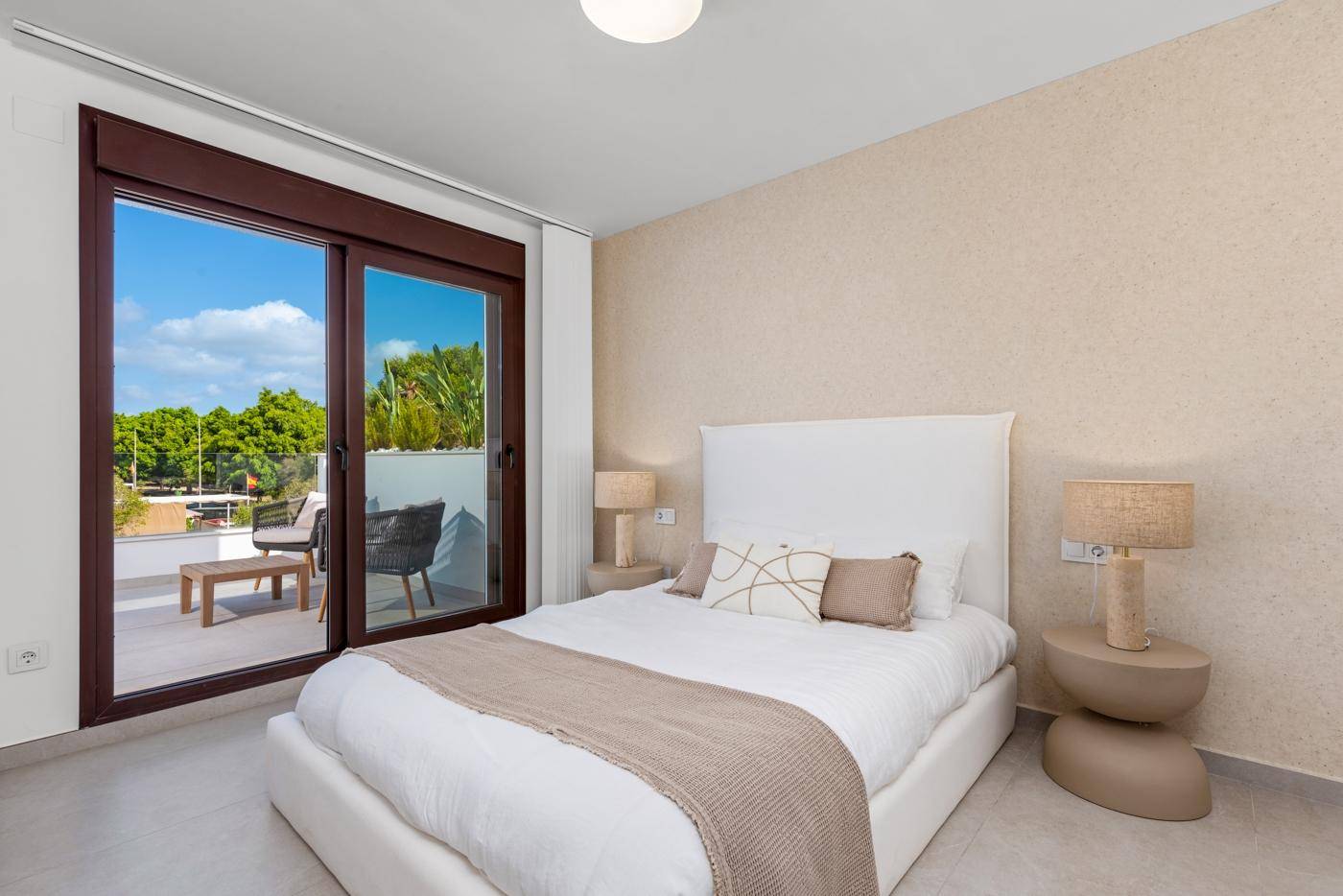 Helles Schlafzimmer mit Zugang zu einem möblierten Balkon und Blick ins Grüne.