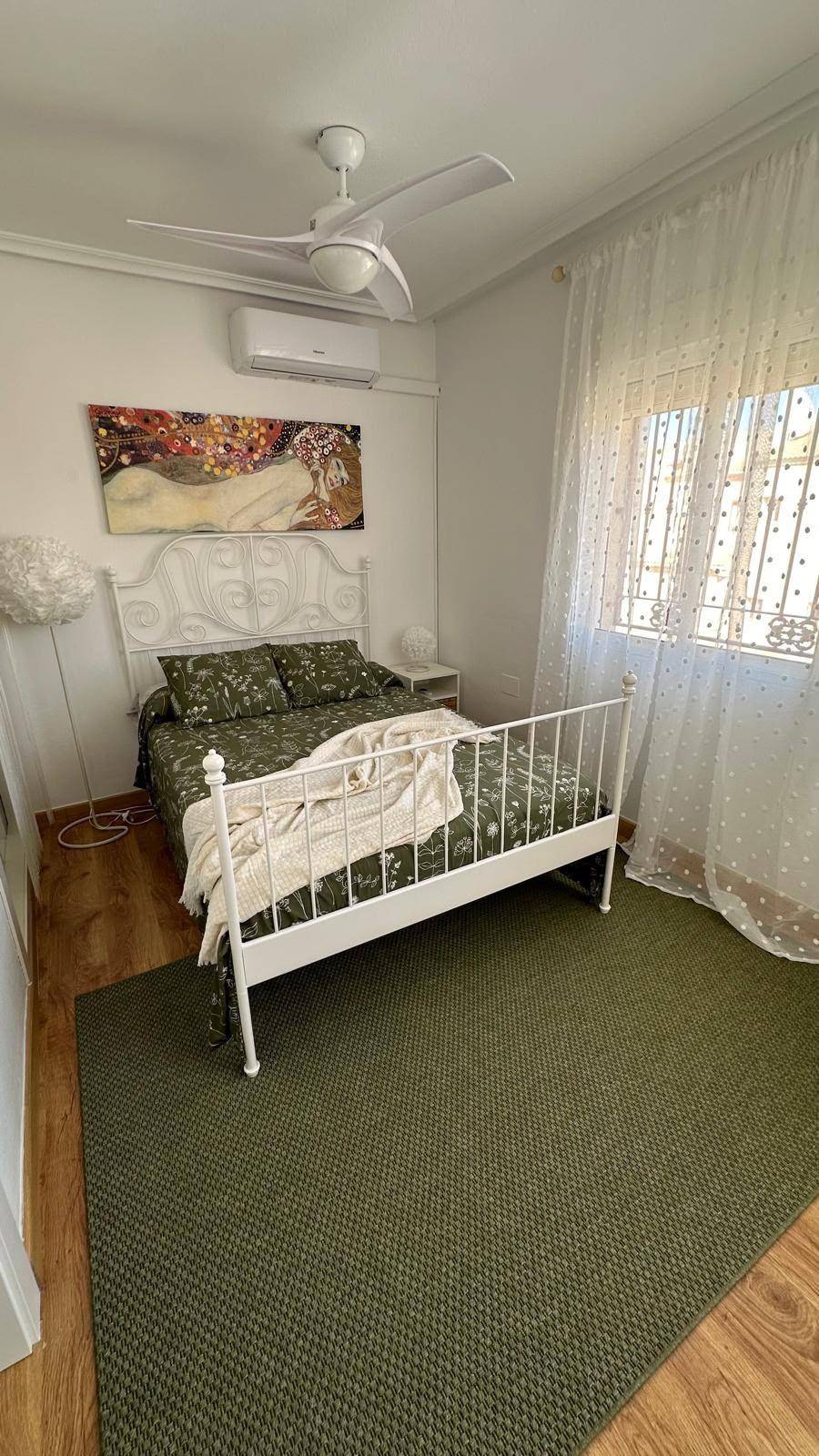 Schlafzimmer mit grünem Teppich, weißem Bett und Deckenventilator, gut beleuchtet.