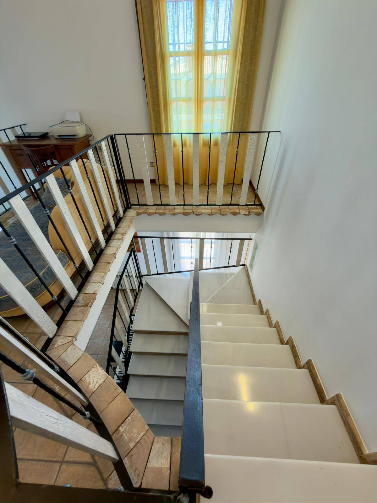 Treppenhaus von oben gesehen mit elegantem Geländer und hellen Stufen.