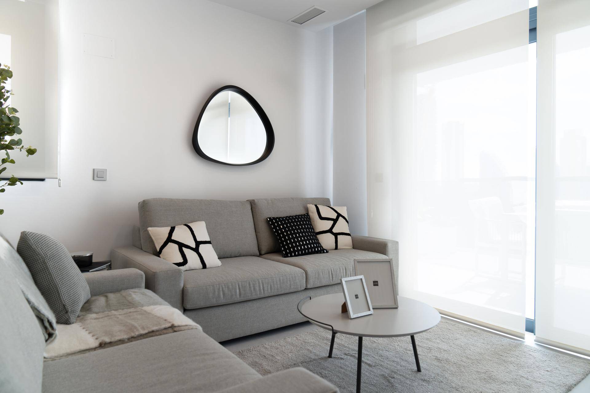 Modern eingerichtetes Wohnzimmer mit grauem Sofa, Teppich und einem runden Spiegel.