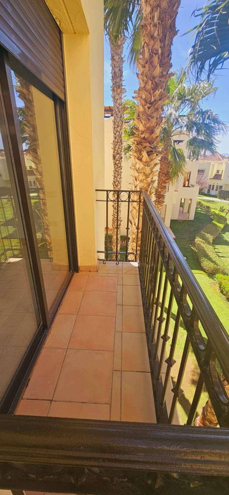 Kleiner Balkon mit Fliesenboden und schmiedeeisernem Geländer, umgeben von Palmen.