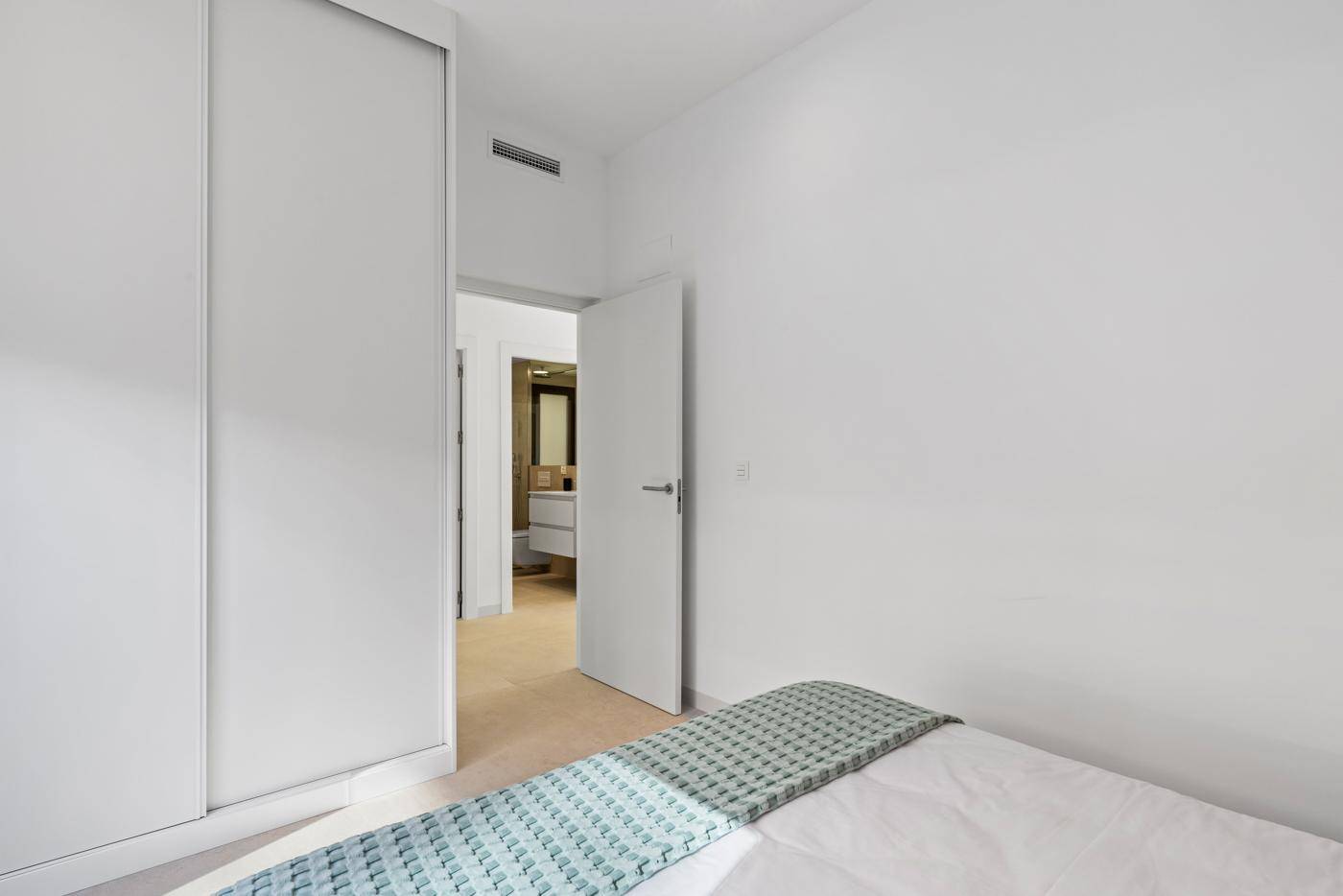 Schlafzimmer mit Einbauschränken und Zugang zu einem modernen Badezimmer.