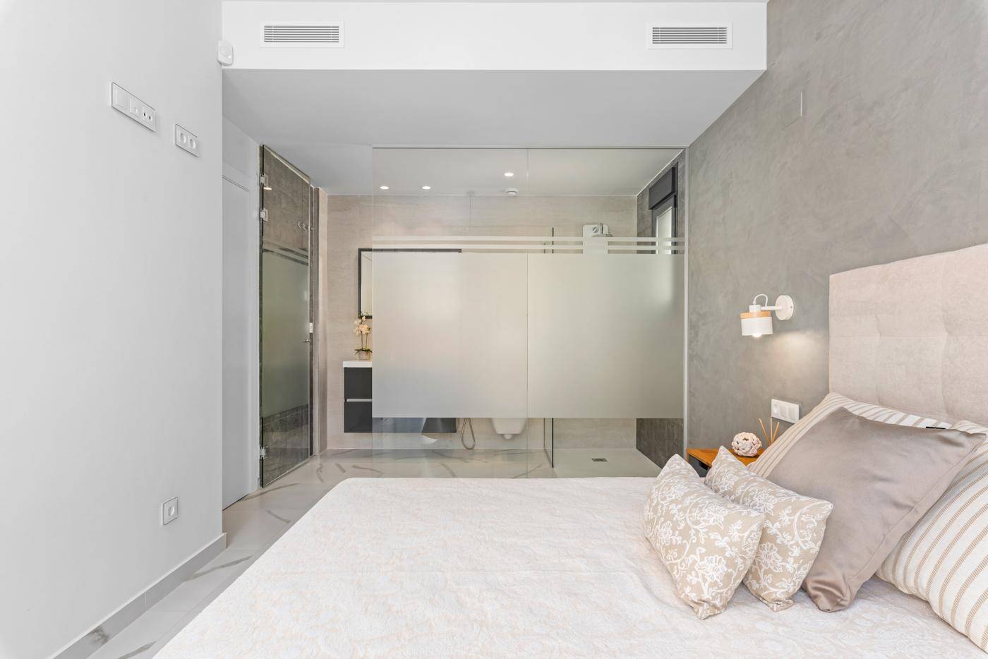 Schlafzimmer mit integriertem Badezimmer, modernen Fliesen und viel Tageslicht.